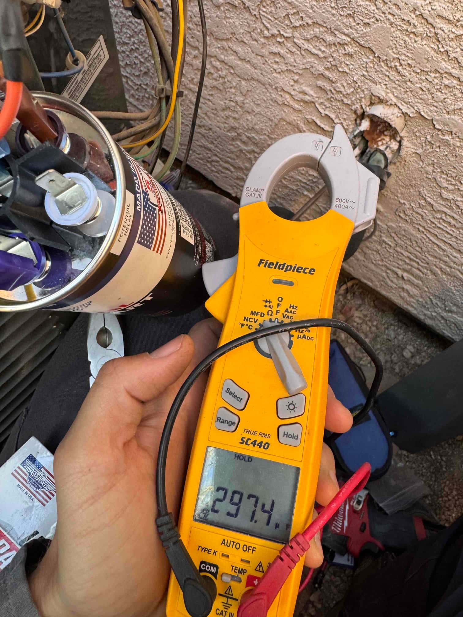 Clamp meter shows 29.74 A on the clamped conductor beside the condenser wiring and dual-run capacitor.
