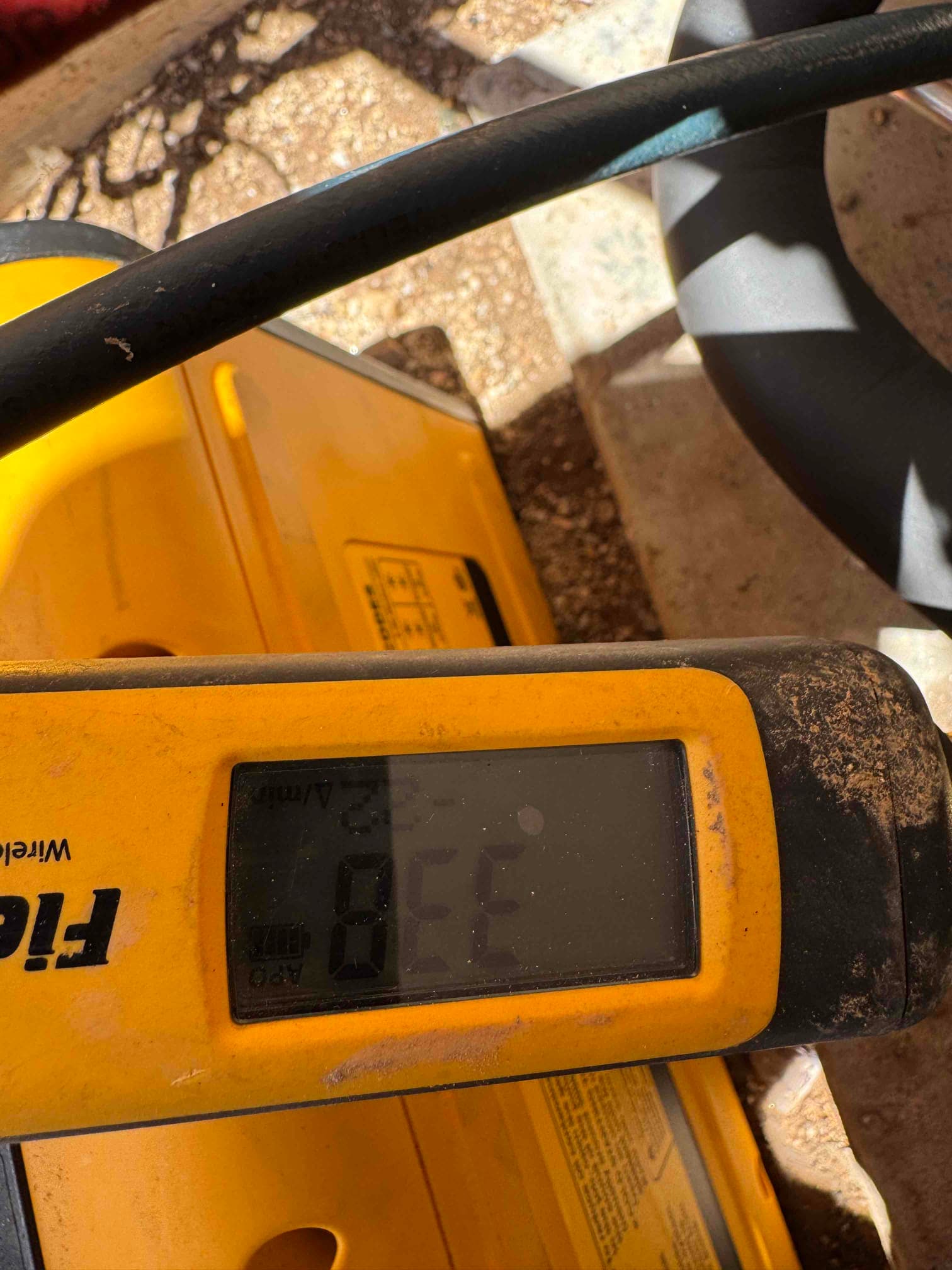 Close-up of a handheld digital meter with an unreadable display on a dusty job site surface.