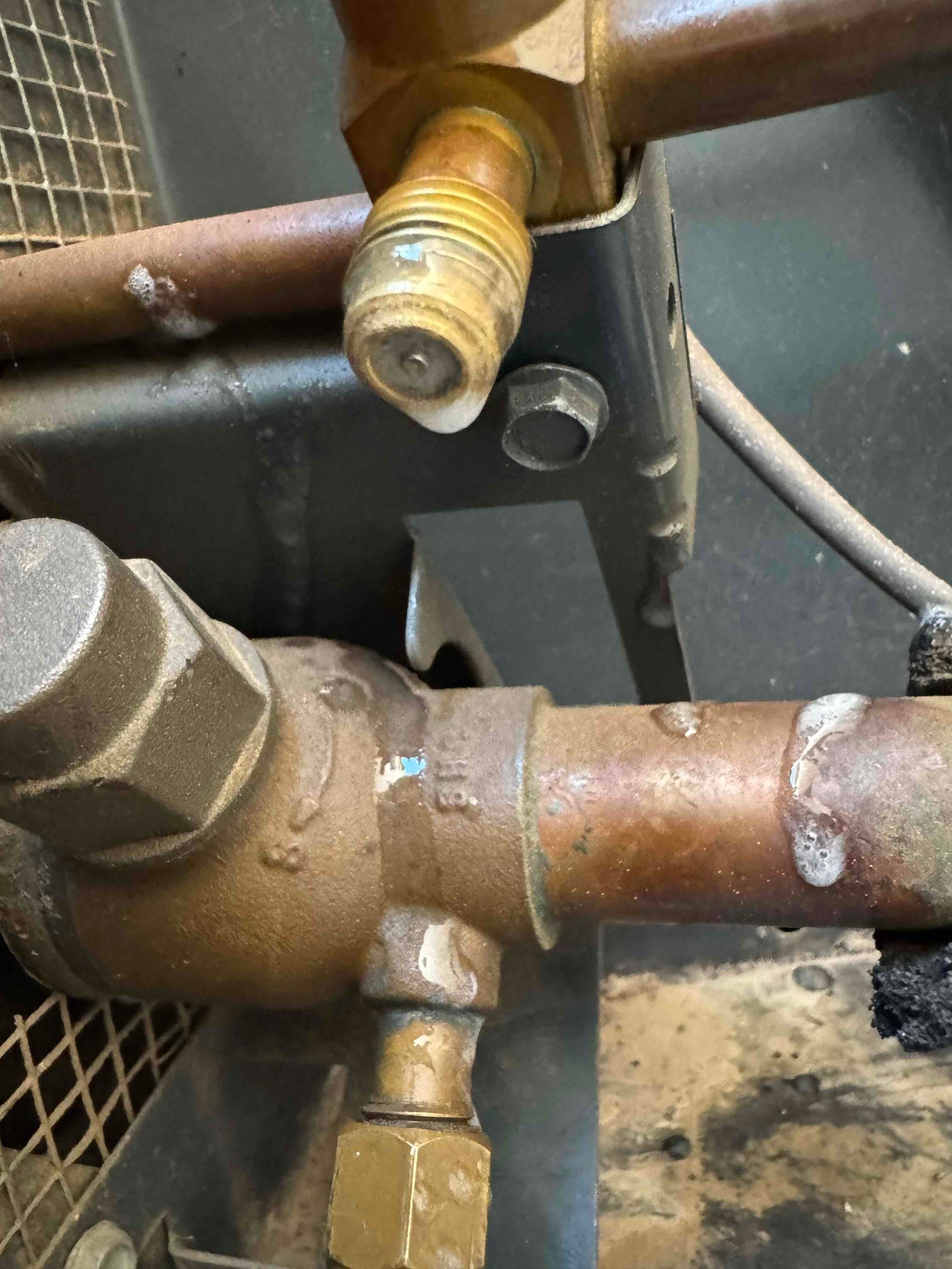 Close-up of refrigerant service valve and copper tubing inside the condenser, showing threaded caps and brazed joints.