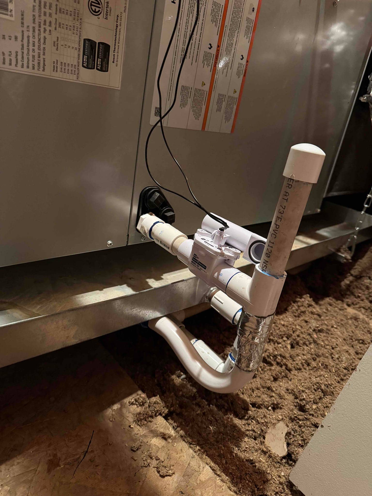 Condensate drain assembly at the air handler, showing PVC piping, cleanout tee, water sensor float switch, and glued connections.