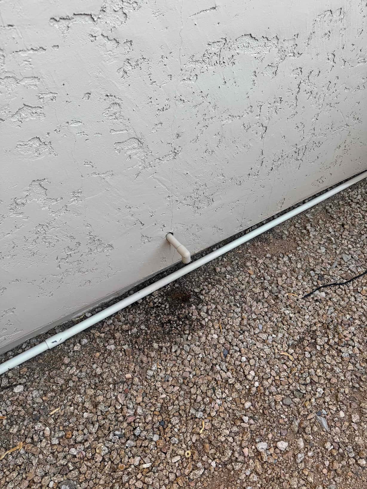 Condensate drain line terminates through the exterior wall above gravel, showing clean outlet and intact PVC piping.
