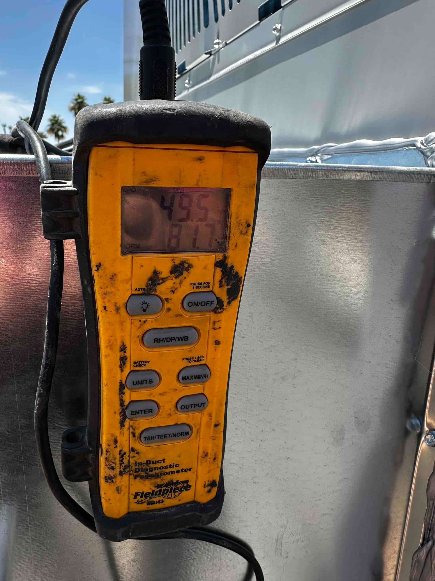 Digital duct diagnostic thermometer displays 49.5°F, documenting cold supply air temperature at the outdoor unit connection.