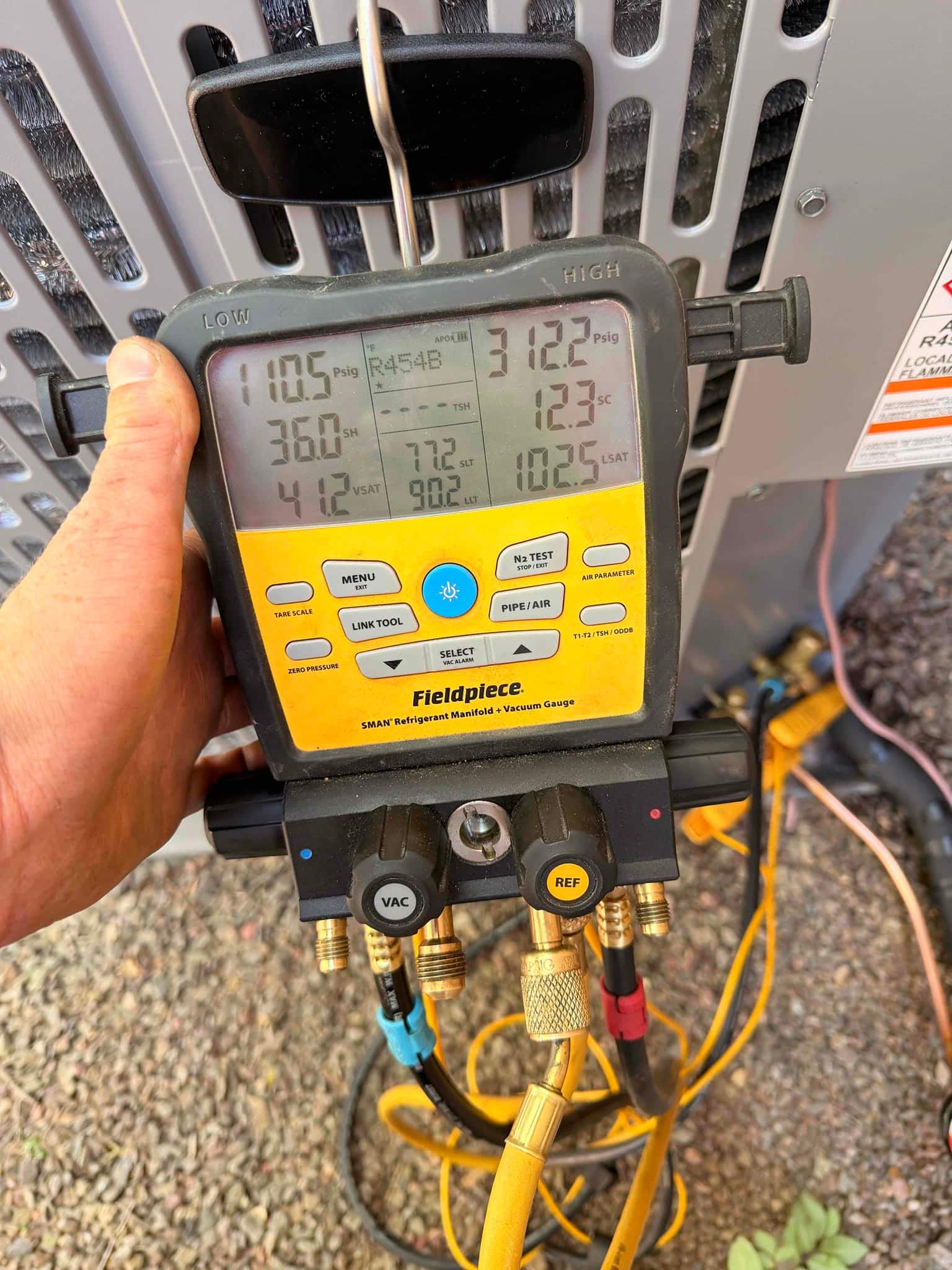 Digital manifold connected to outdoor unit shows operating pressures and temperatures during system commissioning.