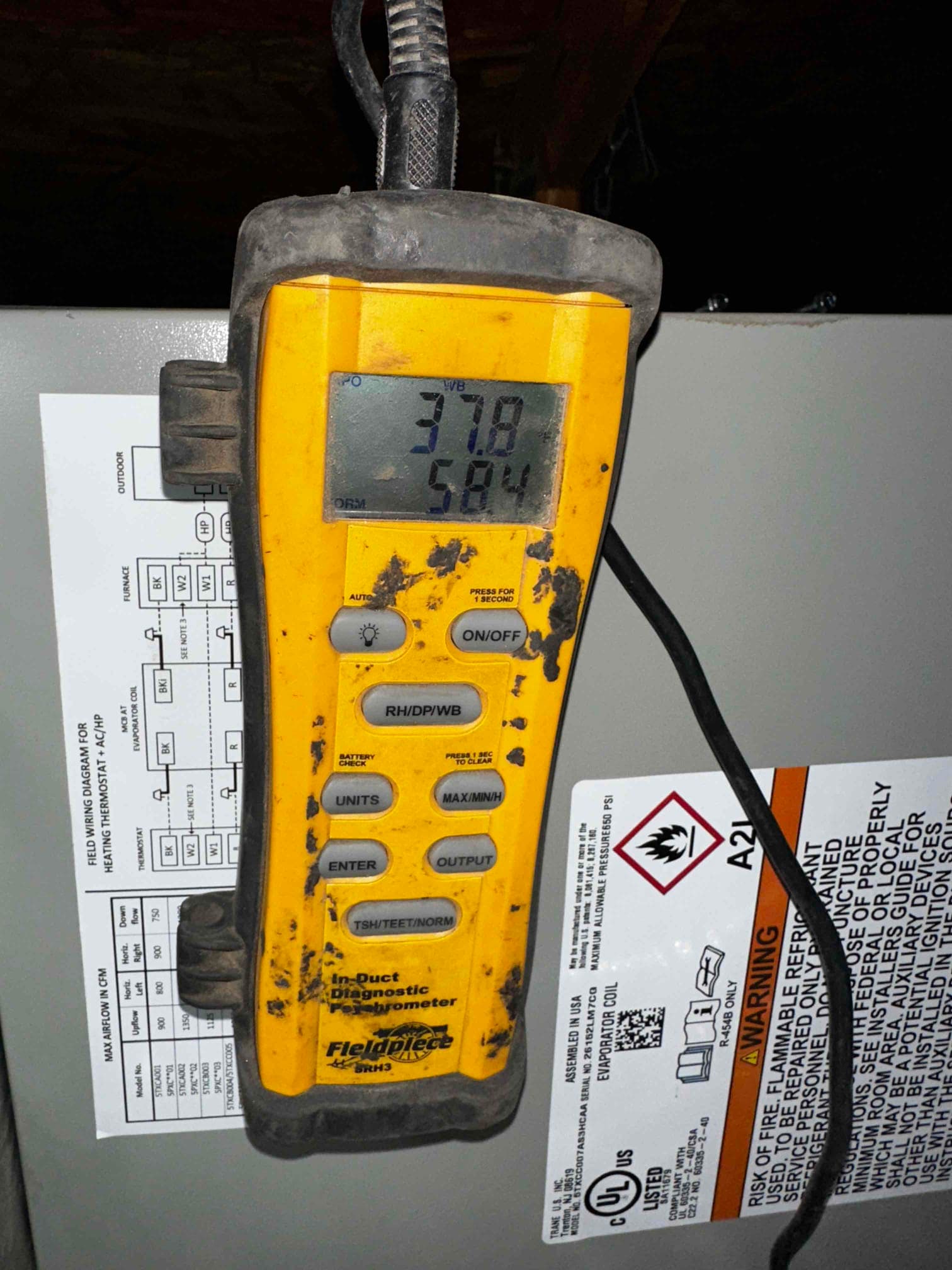 Digital psychrometer displays 37.8 and 58.4 while measuring air conditions near the air handler during commissioning.