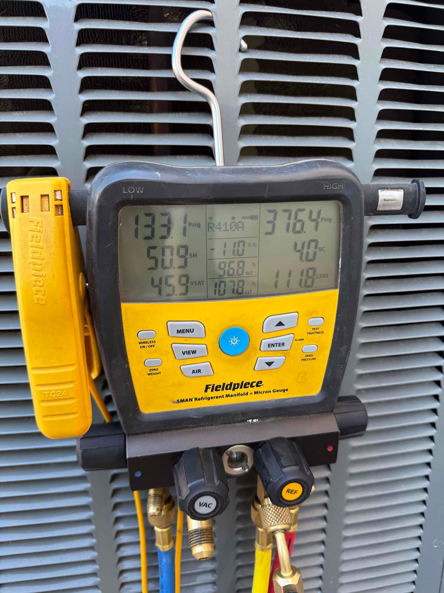 Digital refrigerant manifold gauge on an outdoor condenser shows low-side 133.1 psi and high-side 376.4 psi with R410A selected.