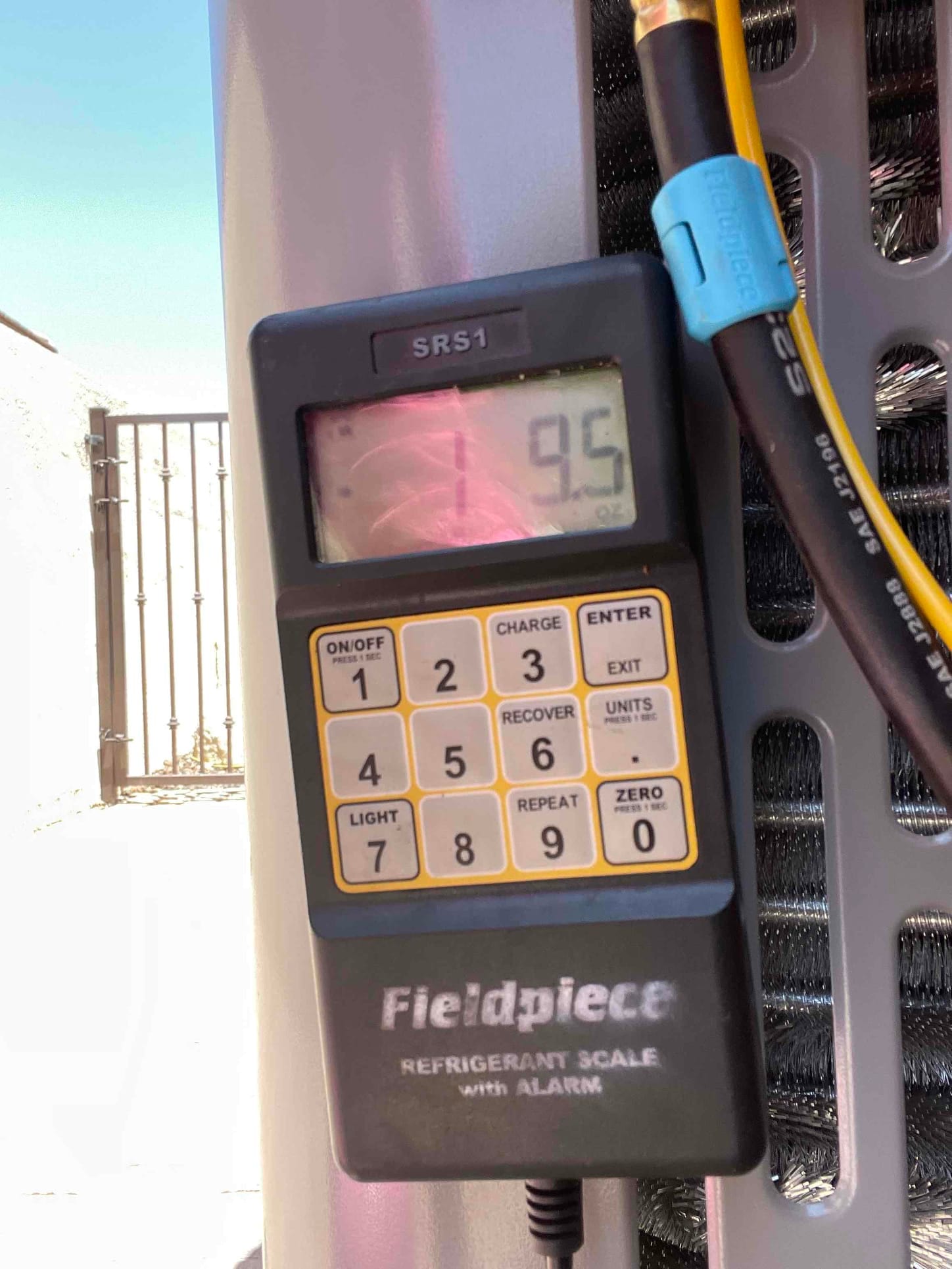 Digital refrigerant scale displays 9.5 ounces during charging beside the outdoor condenser cabinet.