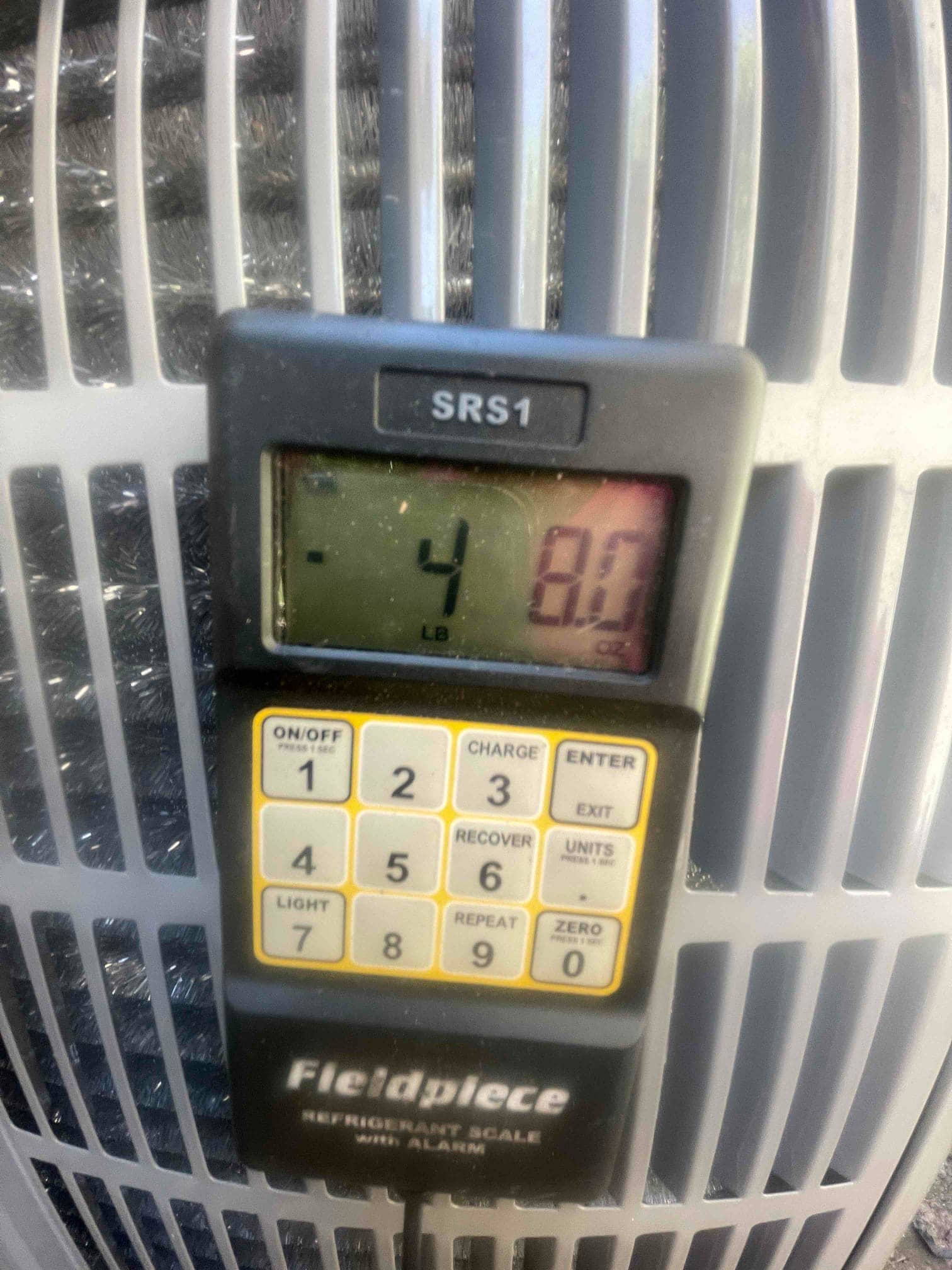 Digital refrigerant scale displays a weight reading during charging at the outdoor condenser.