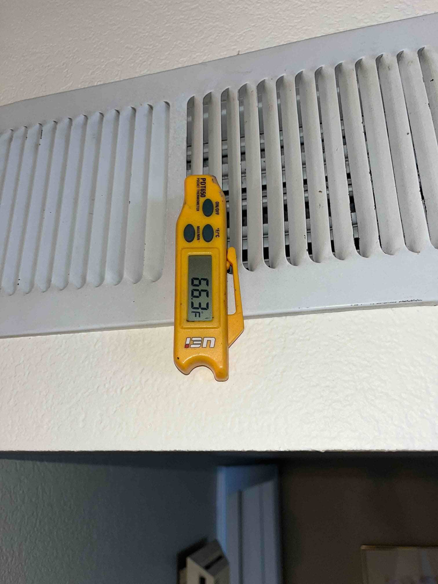 Digital thermometer at a ceiling supply register shows 39.9 °F supply air temperature during air conditioning operation.