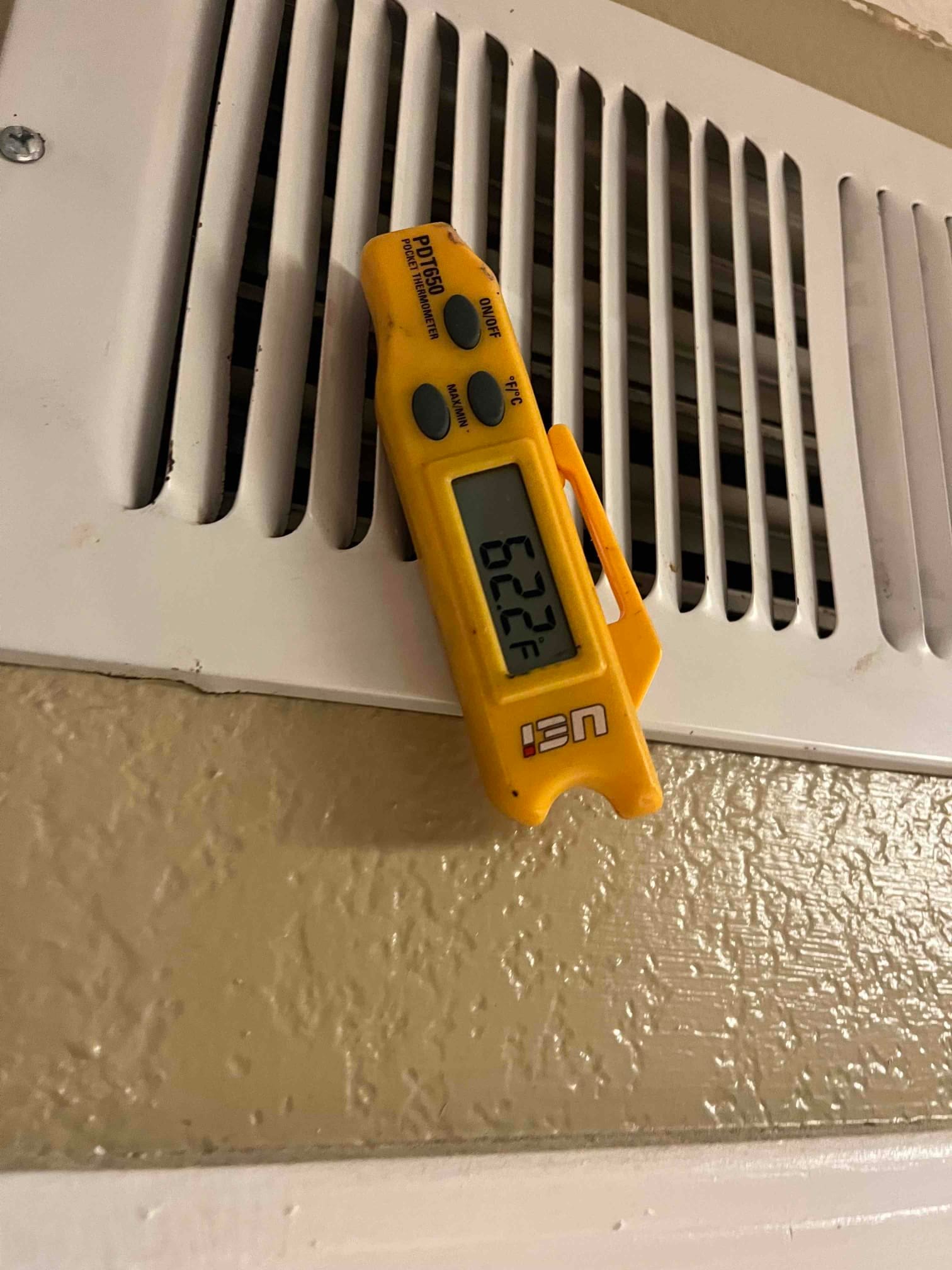 Digital thermometer clipped to a supply register shows 62.2 °F supply air temperature during operation.