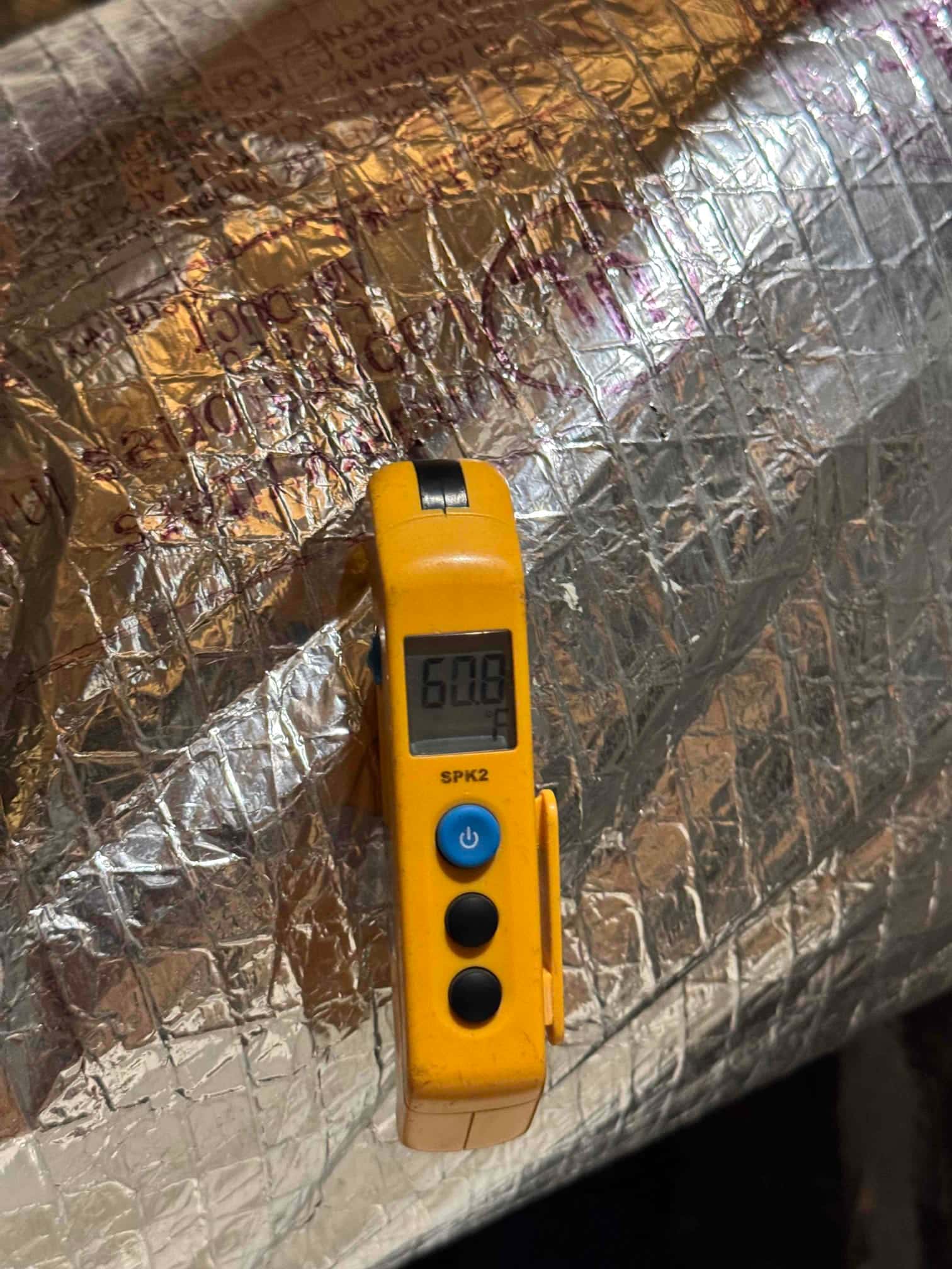 Digital thermometer displays 60.8 °F while measuring air temperature at the insulated duct surface.