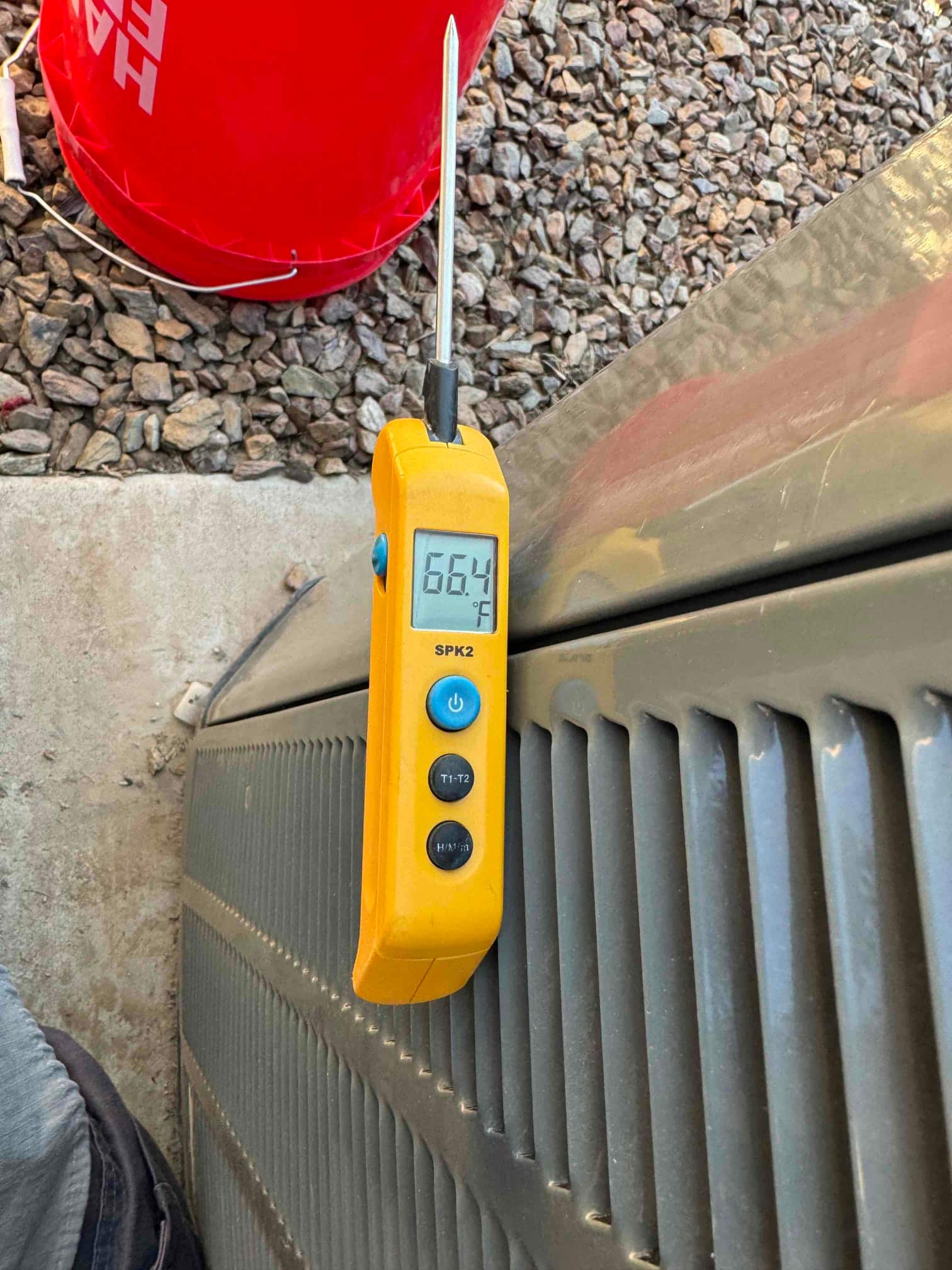 Digital thermometer displays 66.4 °F with probe inserted, positioned on top of the outdoor condenser housing.