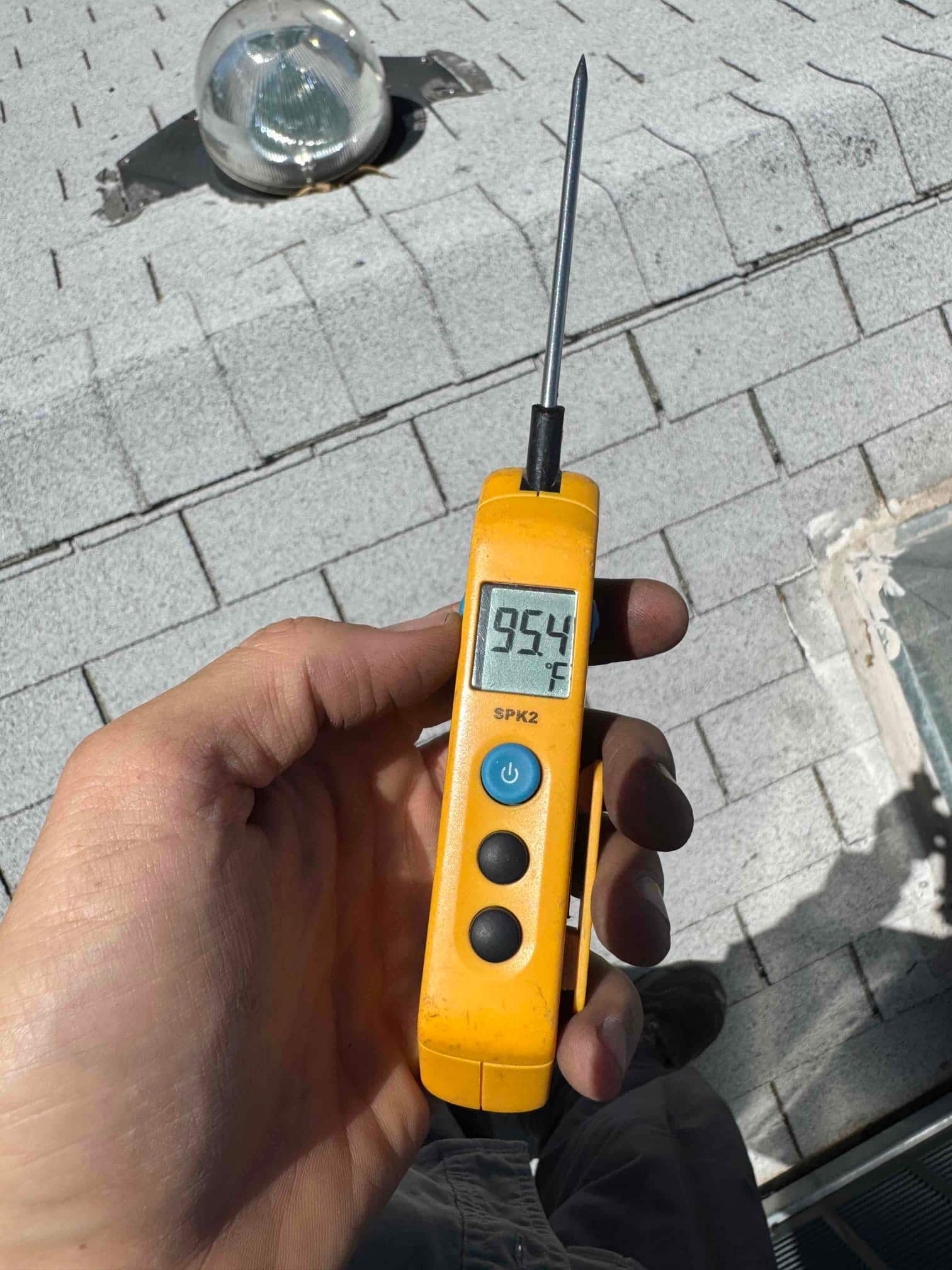 Digital thermometer displays 95.4 °F with the probe extended, held by the technician on a rooftop near HVAC equipment.