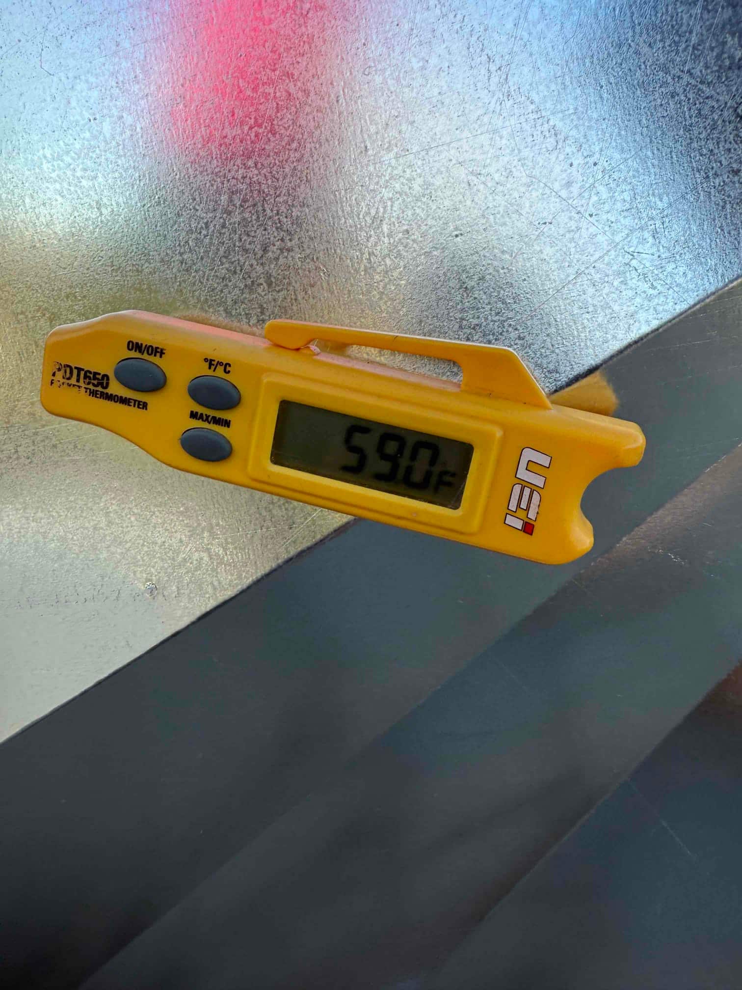 Digital thermometer on duct surface shows 59°F, documenting supply air temperature after cooling operation.