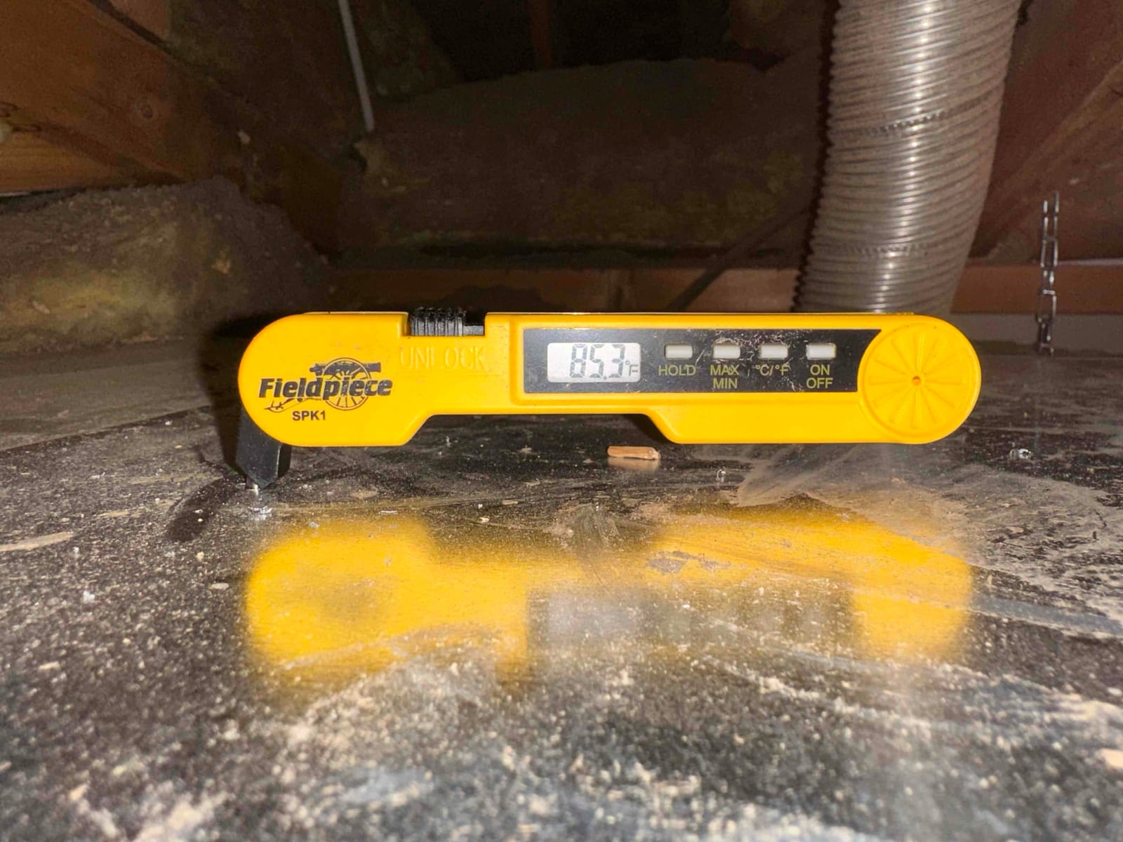 Digital thermometer on duct surface shows 85°F, documenting air-side temperature during commissioning in the attic space.