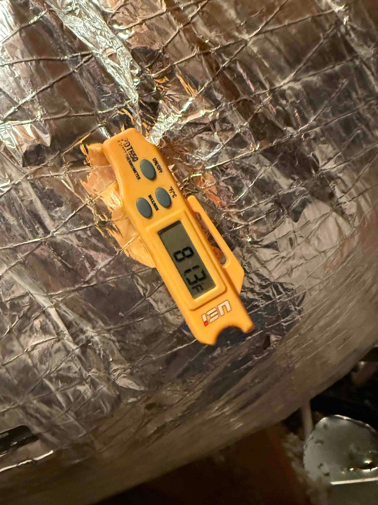 Digital thermometer inserted into insulated duct shows 80.3°F, documenting a return air temperature reading during commissioning.
