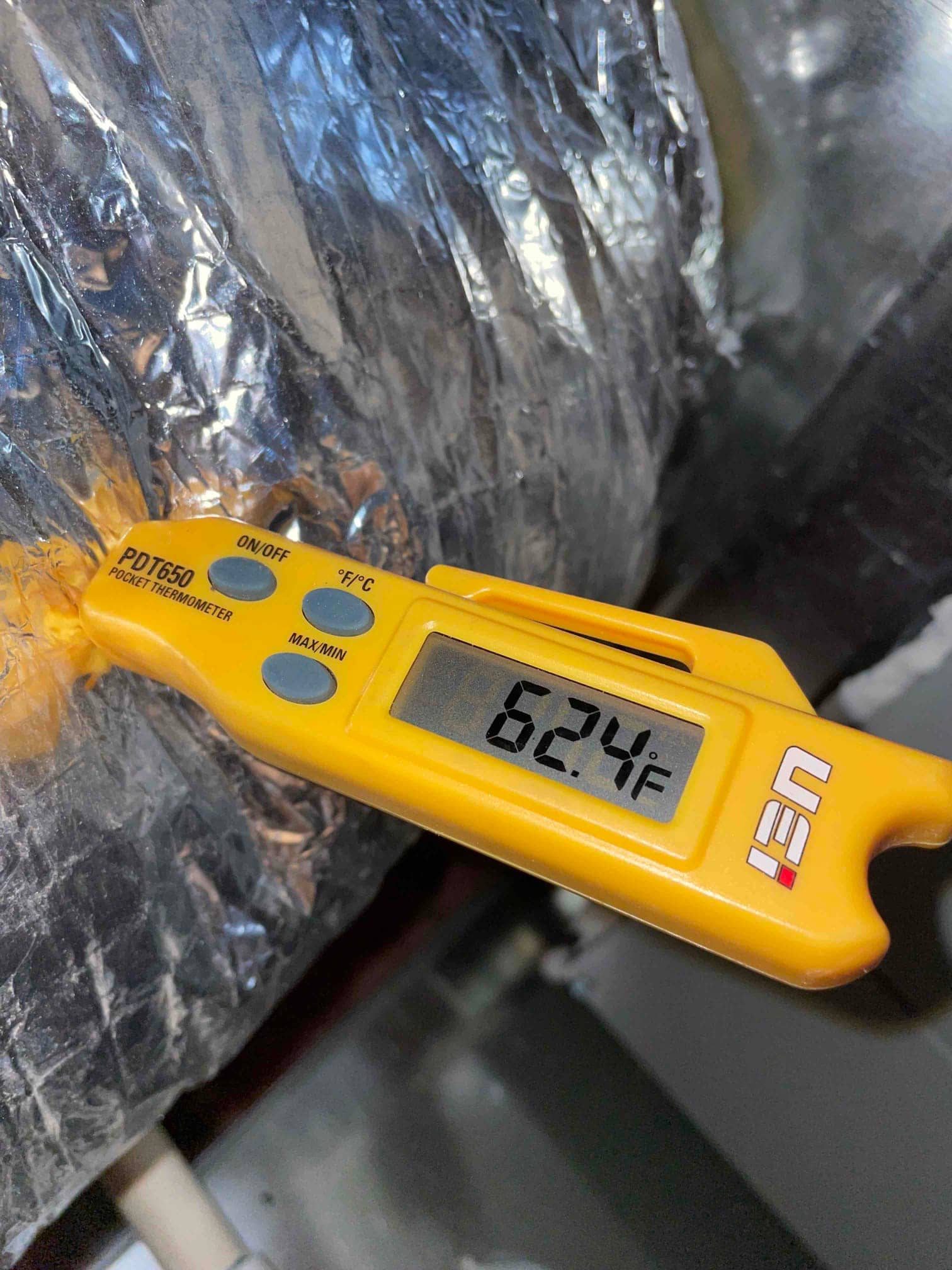 Digital thermometer probe measures 62.4°F on insulated ductwork, documenting supply air temperature during cooling operation.