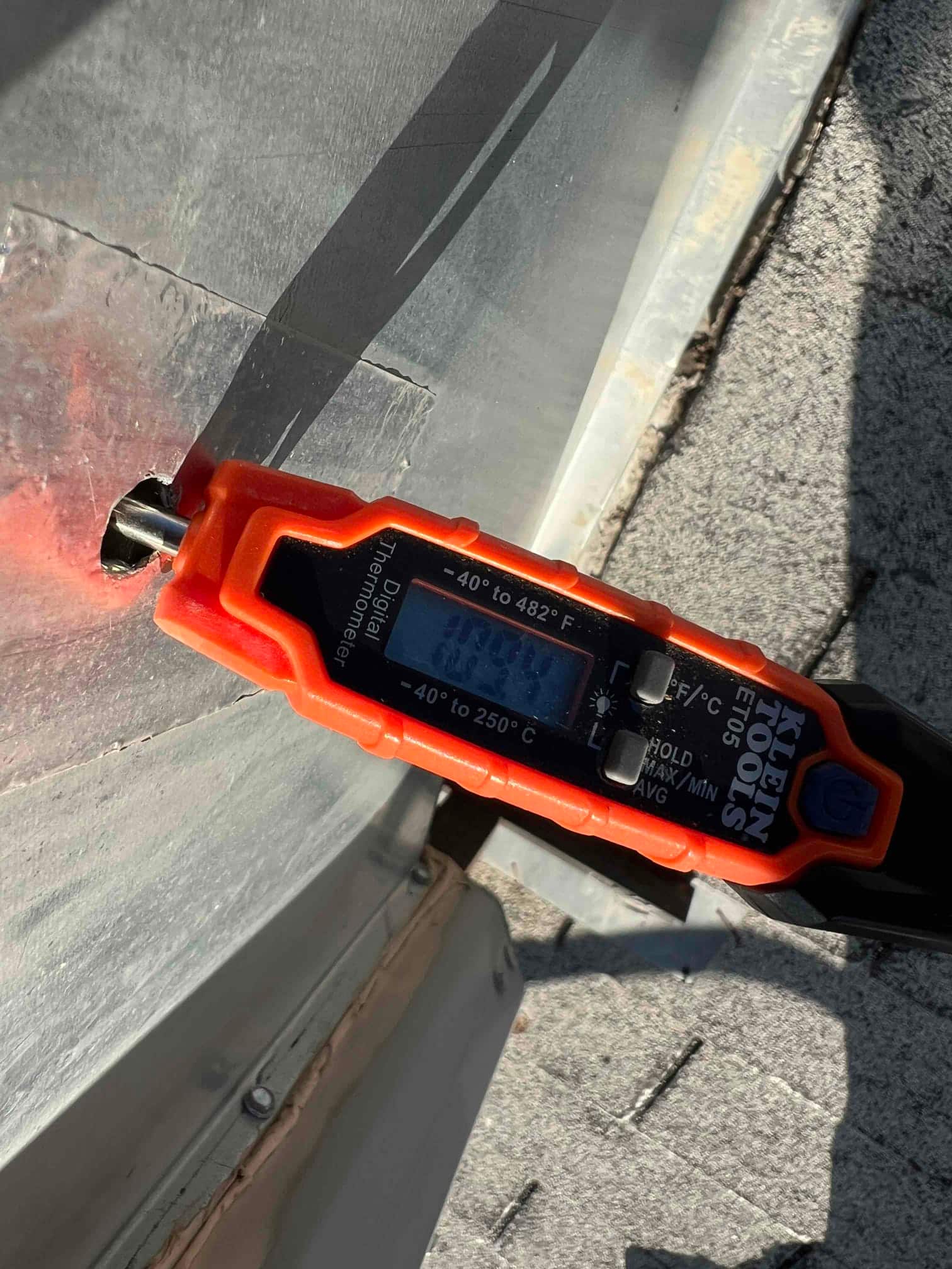 Digital thermometer probe measures surface temperature at a metal housing, displaying 102.7 °F on the meter screen.
