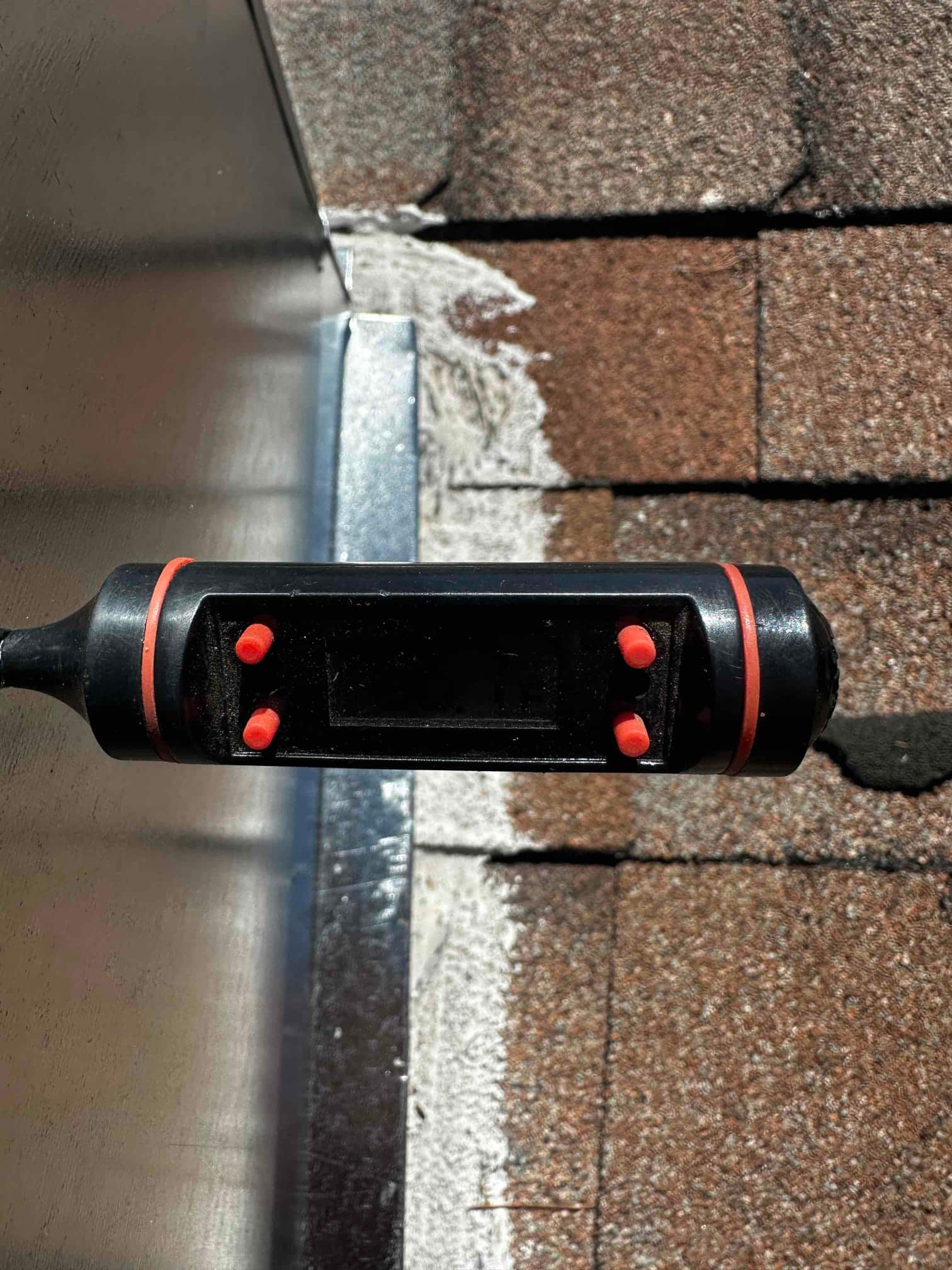 Digital thermometer probe positioned at a rooftop duct or curb, but the display is not readable in direct sunlight.