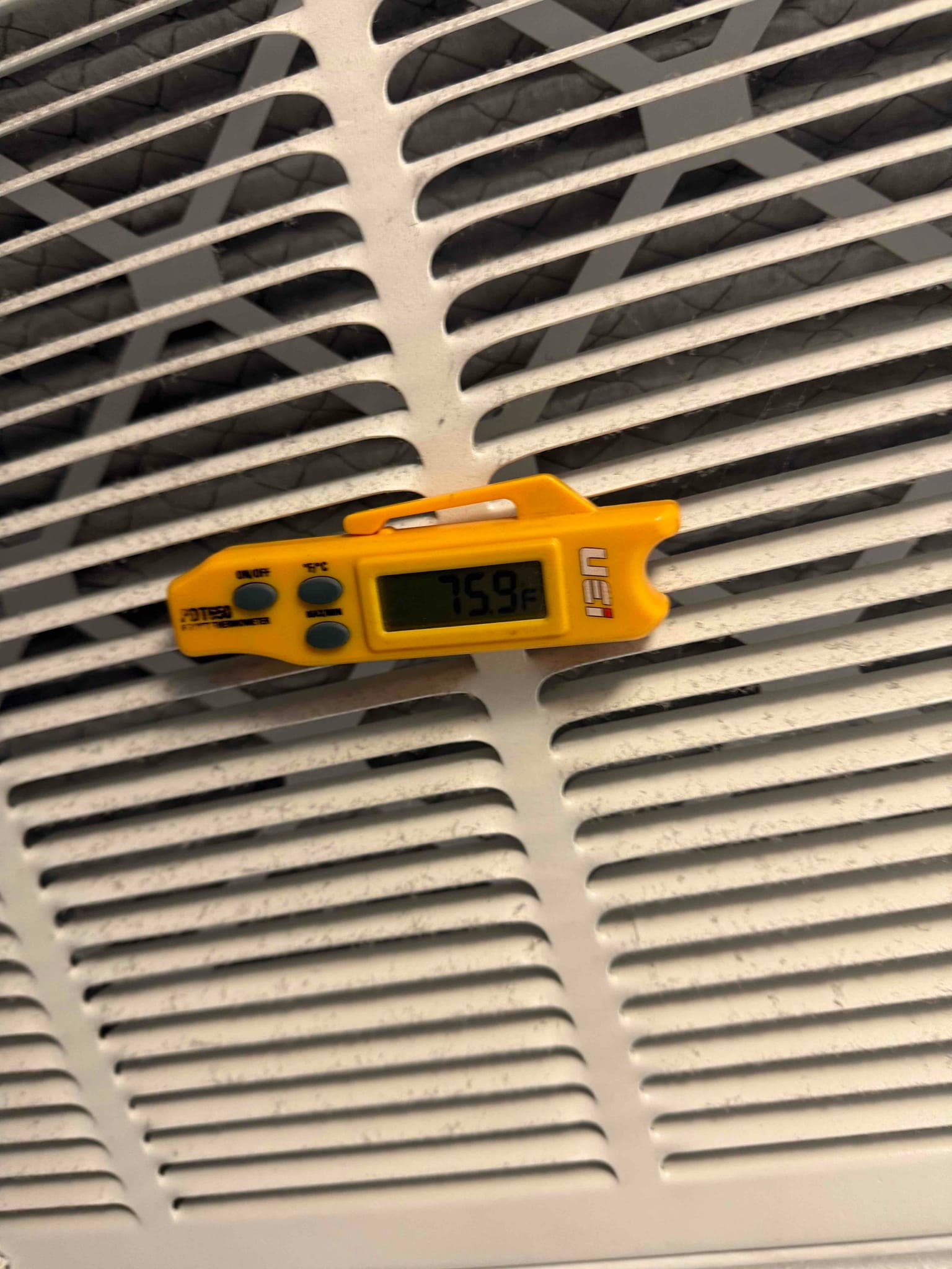Digital thermometer on a return grille shows 75.9°F, documenting return air temperature during system commissioning.