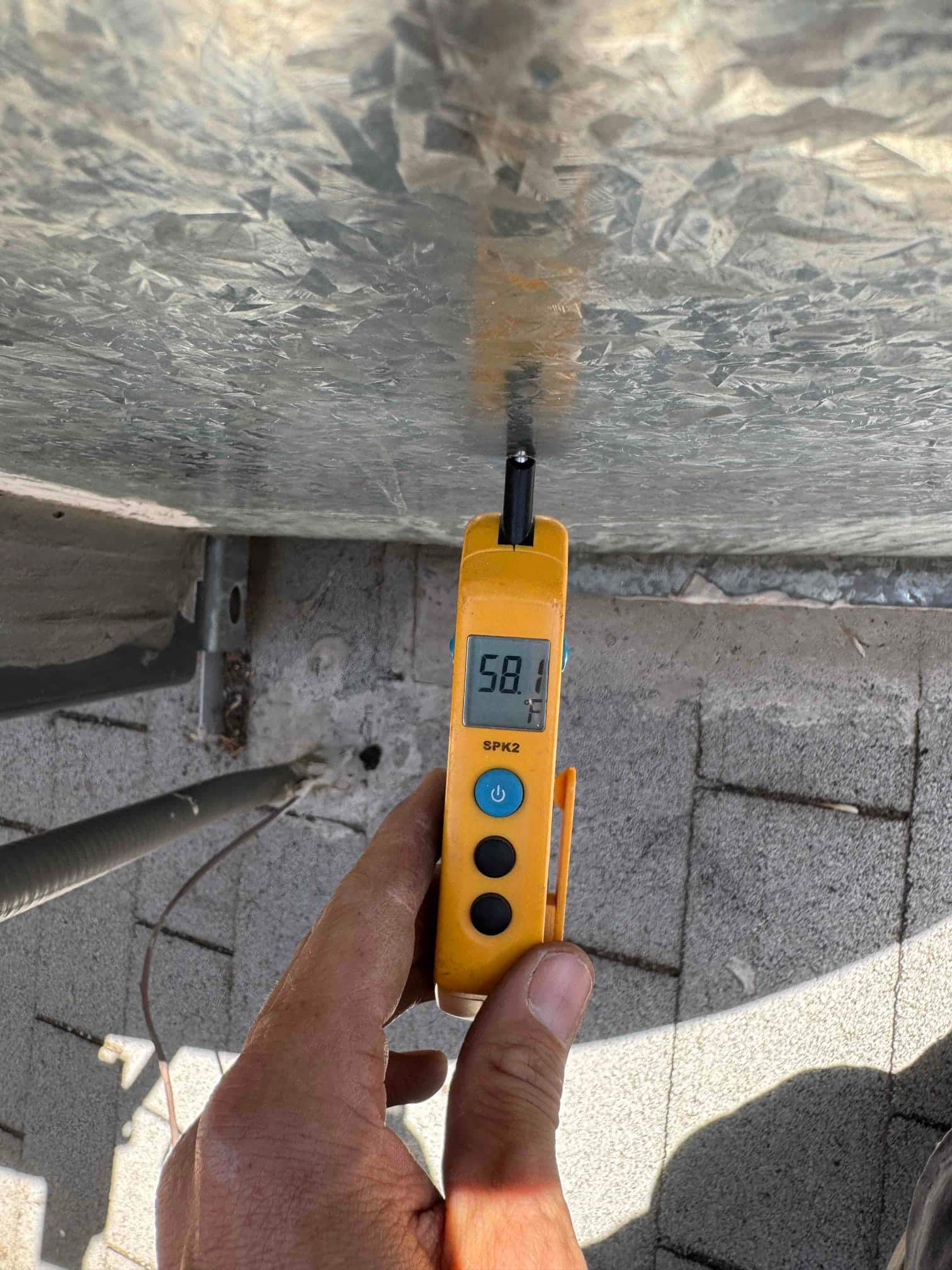 Digital thermometer shows 58.1 °F while measuring the surface temperature of a galvanized HVAC duct or panel.