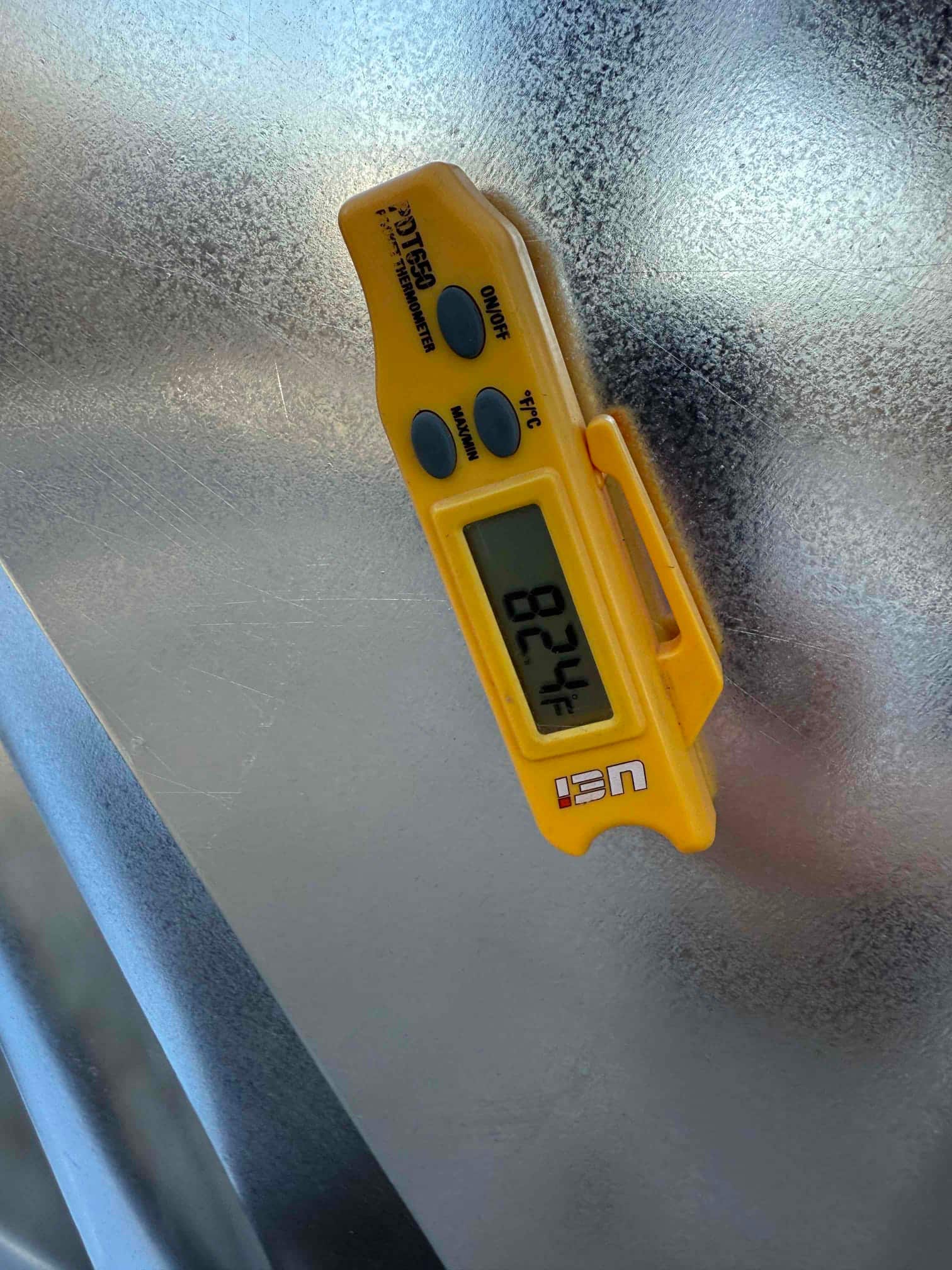 Digital thermometer shows 82.4°F while checking air temperature at the duct during commissioning.