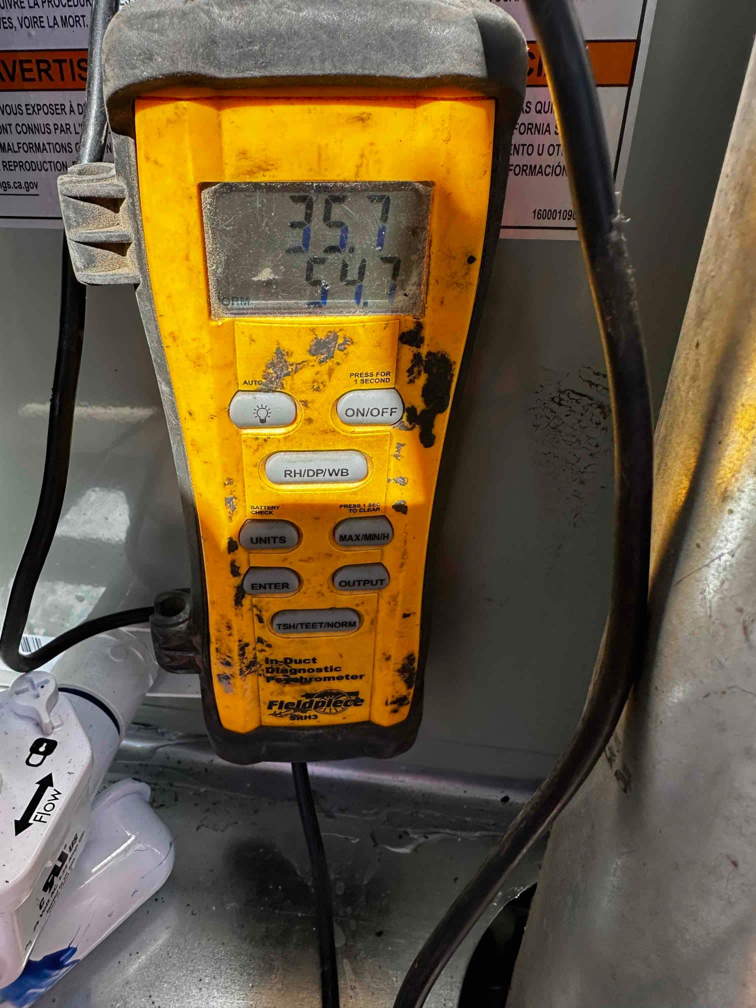 Digital thermometer shows air temperatures of 35.7 and 54.7 degrees during duct temperature measurements at the indoor unit.