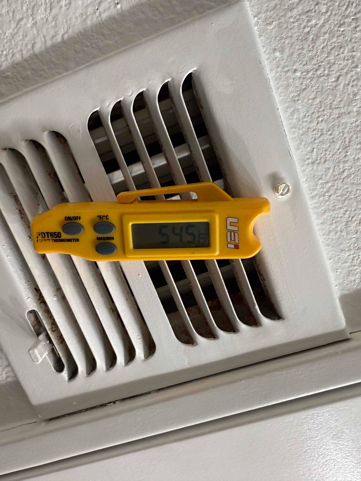 Digital thermometer at a supply register reads 54.5°F, documenting cooled air temperature leaving the evaporator.