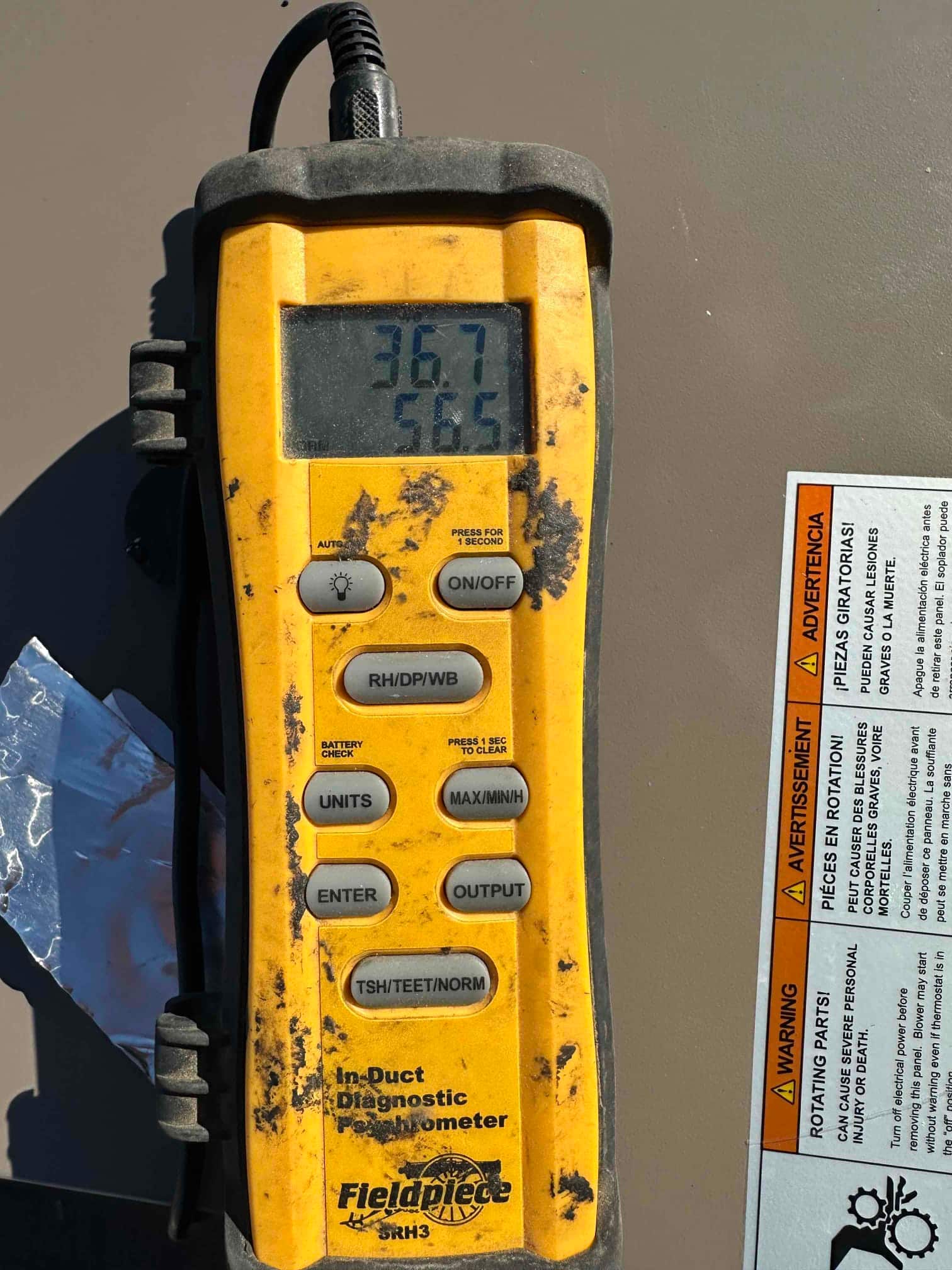 Digital thermometer used during commissioning shows 56.5 degrees, indicating cooled supply air temperature from the system.