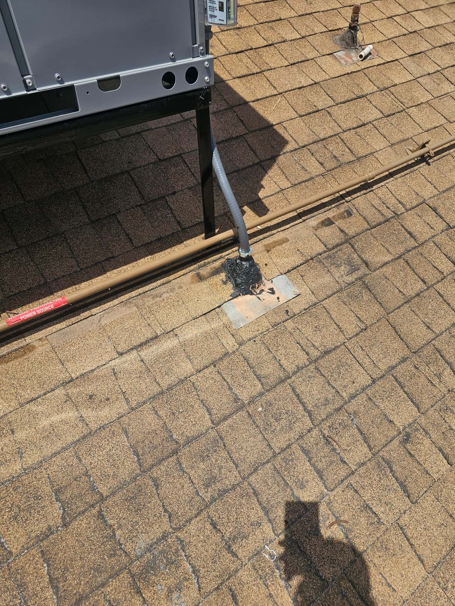Electrical flex conduit neatly routed into the roof penetration beside refrigerant line set near the newly installed rooftop unit.