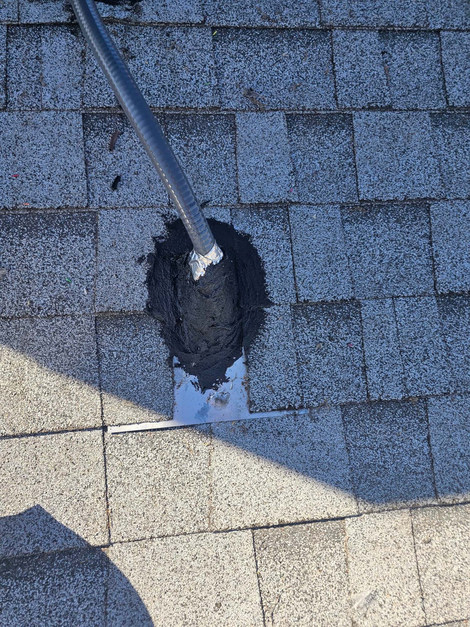 Electrical whip penetration through roof shingles is sealed with flashing and mastic to weatherproof the new HVAC installation.