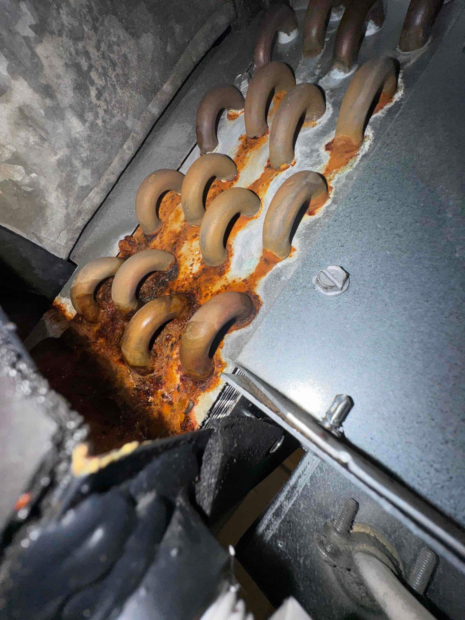Evaporator coil assembly with multiple U-bend joints showing significant rust and corrosion along the drain pan area.