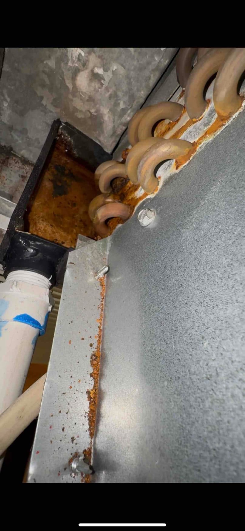 Evaporator coil drain pan area shows rust and standing water near condensate drain piping and corroded metal surfaces.