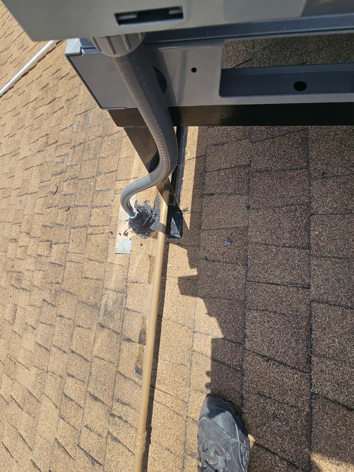 Flexible electrical whip and refrigerant line exiting rooftop penetration beside a mounted outdoor unit stand, sealed at the roof.