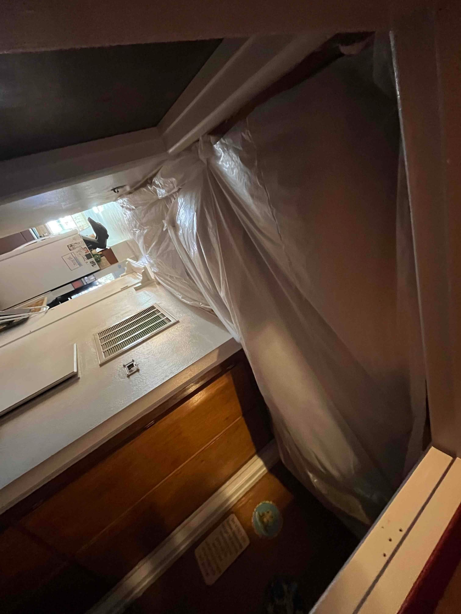 Floor and doorway protected with plastic sheeting near a wall return grille during HVAC installation work.