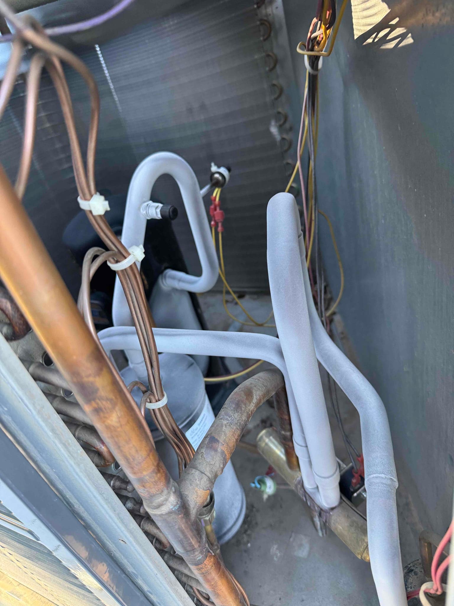 Frosted suction and liquid refrigerant lines inside an outdoor condenser cabinet, with compressor, coil, and wiring visible.