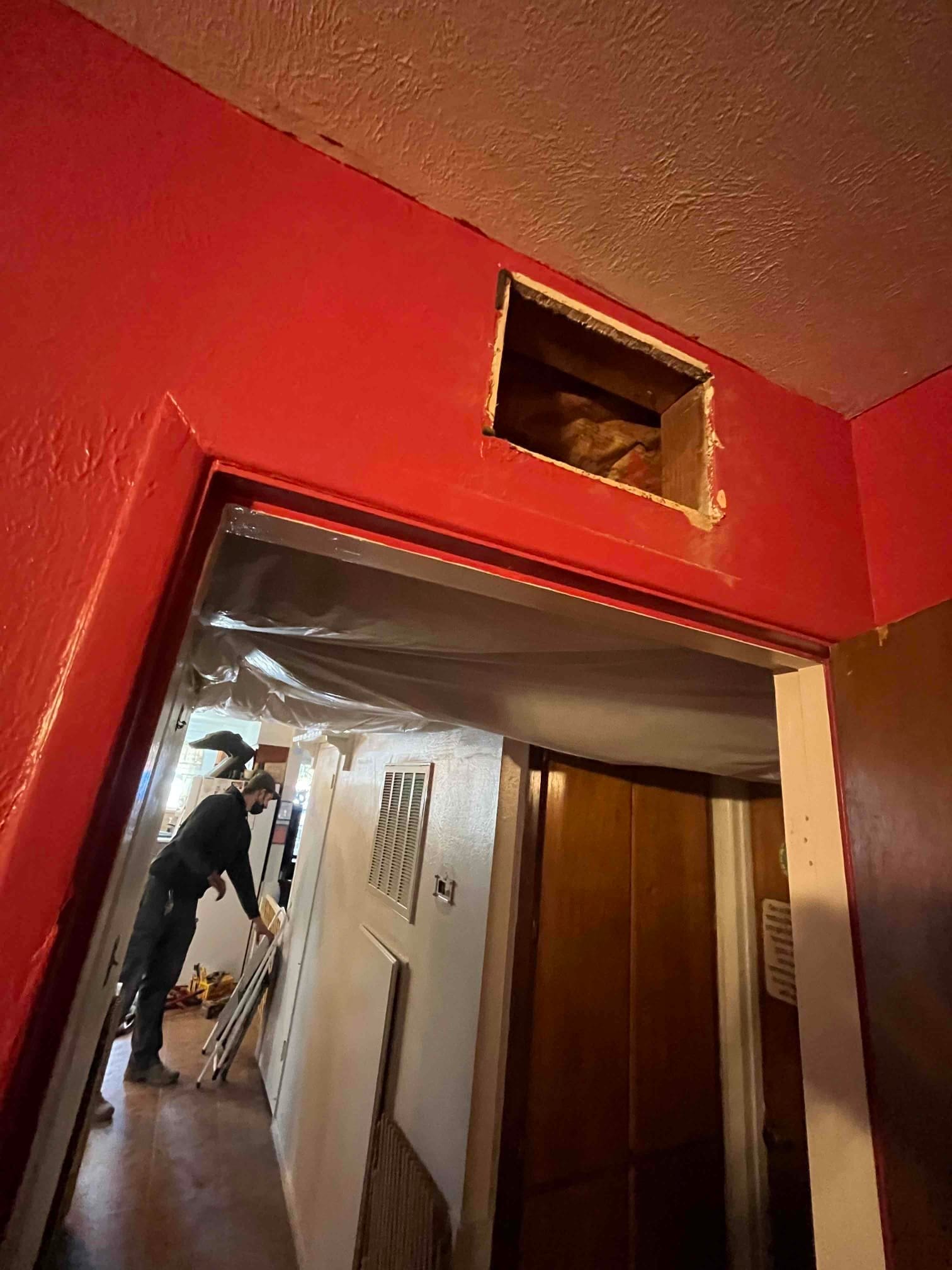Hallway work area with ceiling opening for new duct soffit and return grille removed during HVAC installation.