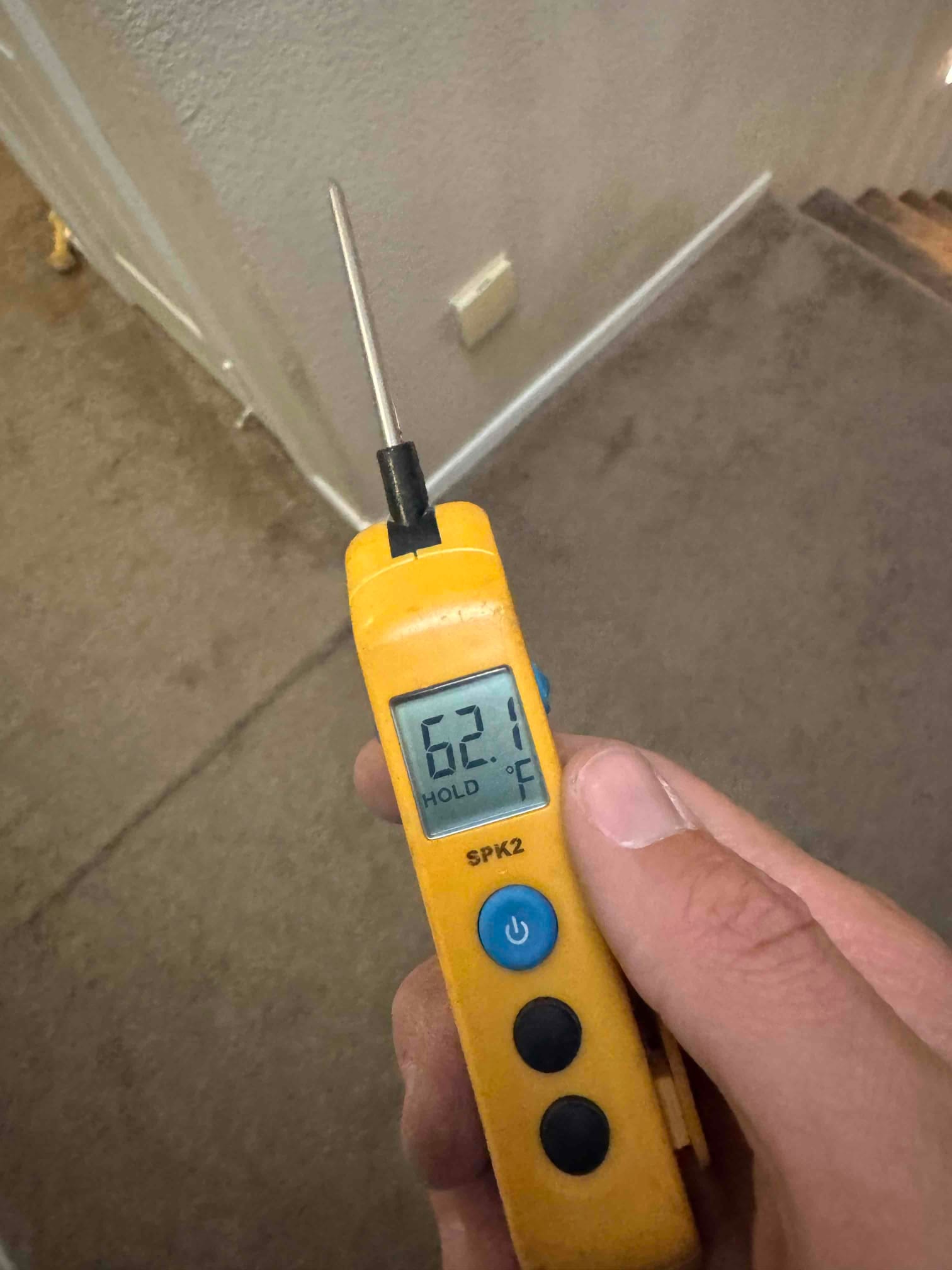 Handheld digital thermometer displays 62.1 °F on the probe while measuring temperature during the air conditioning repair.