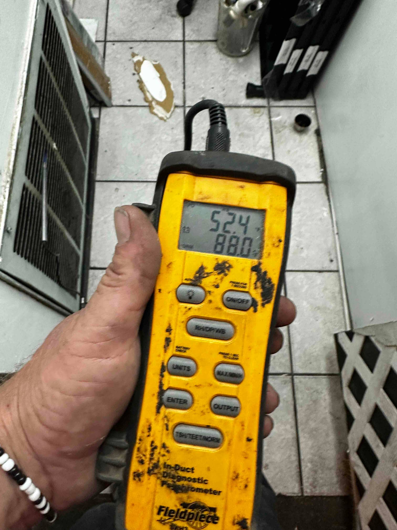 Handheld digital thermometer shows 52.4 degrees in the supply duct during cooling, documenting cold air leaving the evaporator.