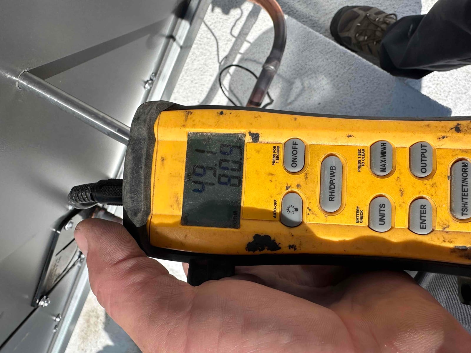 Handheld digital thermometer shows a probe inserted at the unit, displaying an air temperature reading during commissioning.