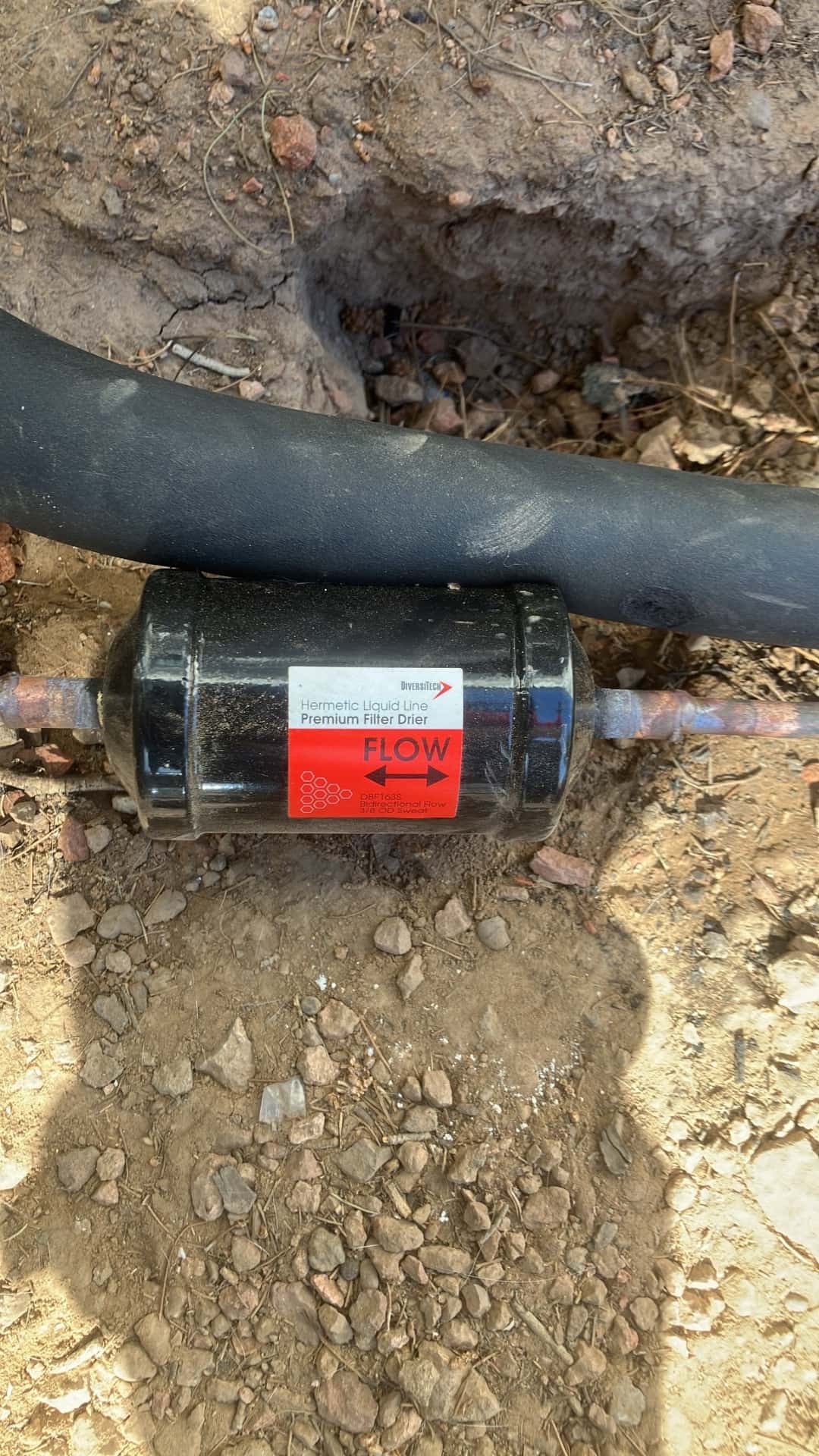 Hermetic liquid-line filter drier installed in the refrigerant circuit with flow direction clearly indicated by the arrow.