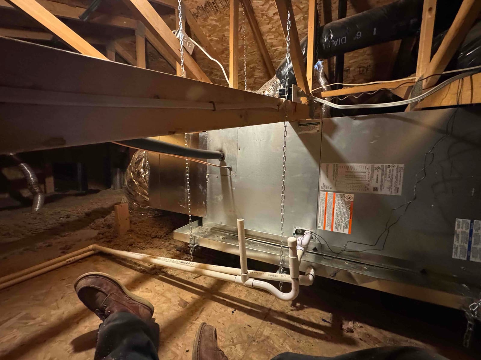 Horizontal air handler suspended on chains in attic with insulated duct connections and newly plumbed condensate trap and drain piping.