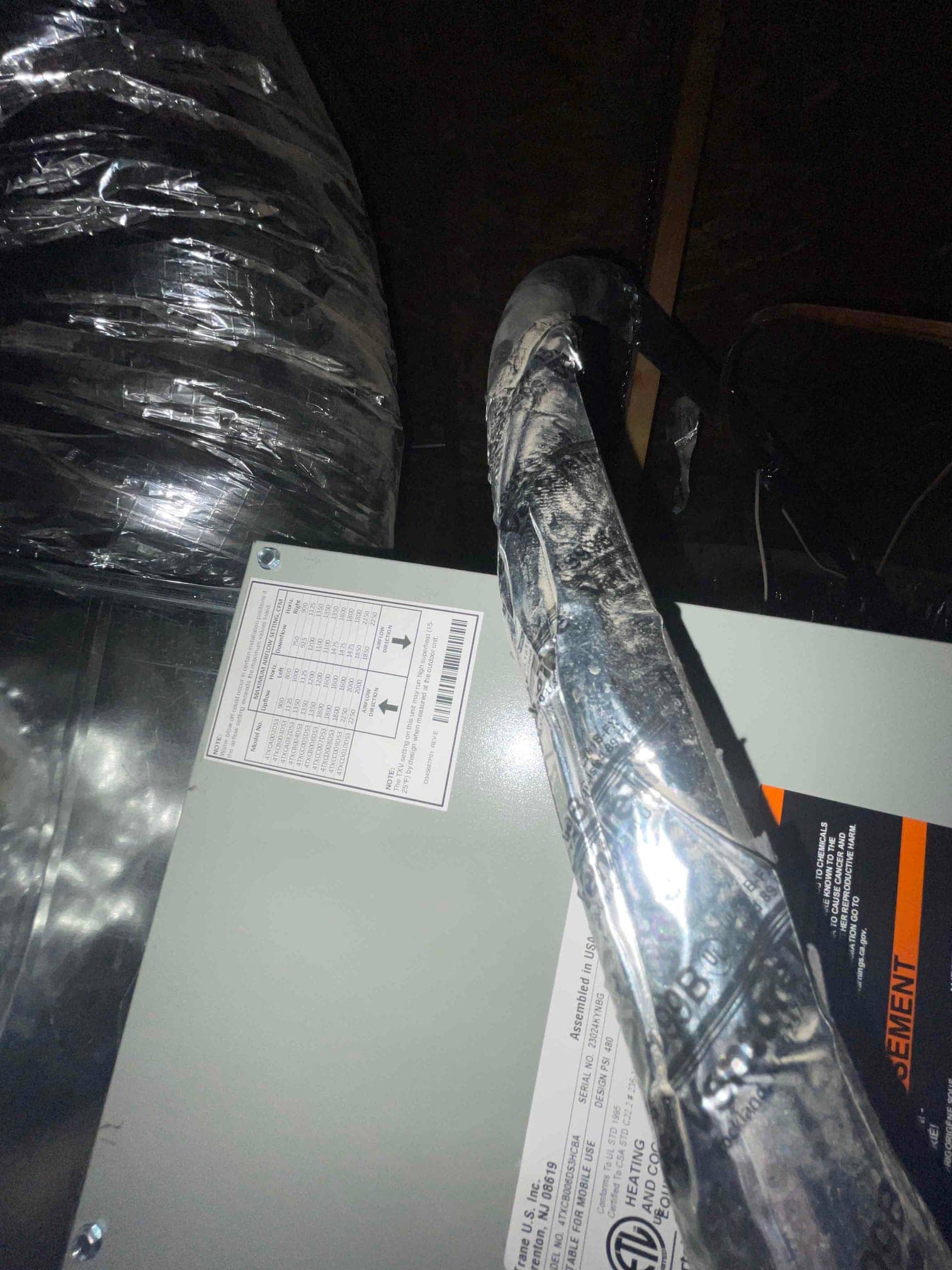 Indoor air handler installed in attic with insulated refrigerant line and flexible duct connection visible.