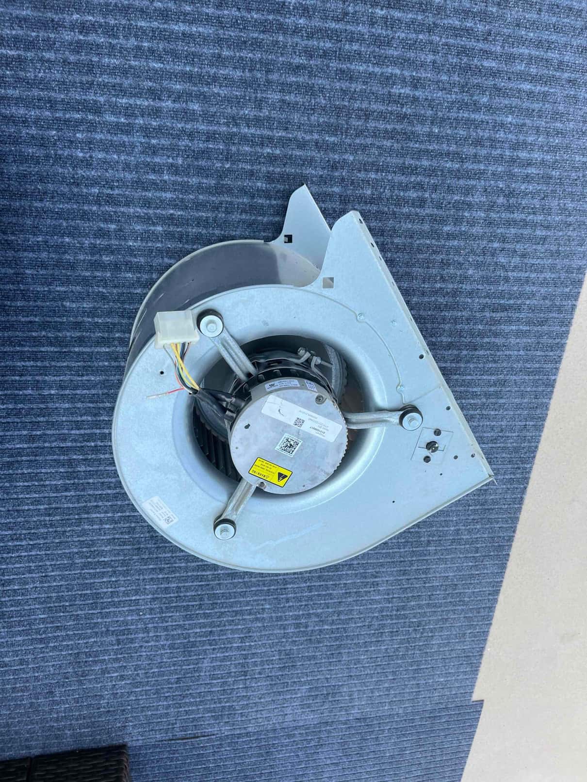 Indoor blower assembly removed, showing new motor pre-wired with mounting brackets and squirrel-cage wheel on a work surface.