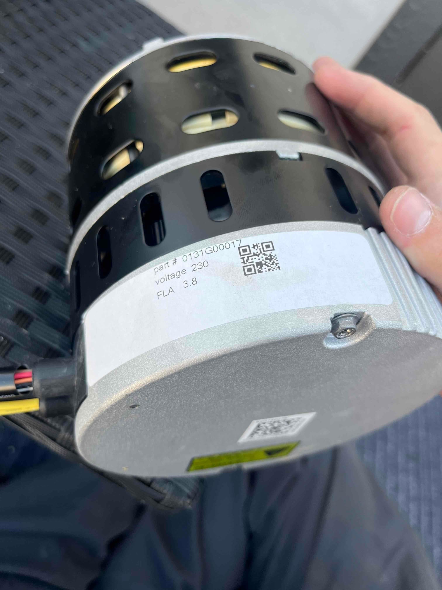 Indoor blower motor being replaced, showing housing vents and printed specs including voltage 230 and FLA 3.8.