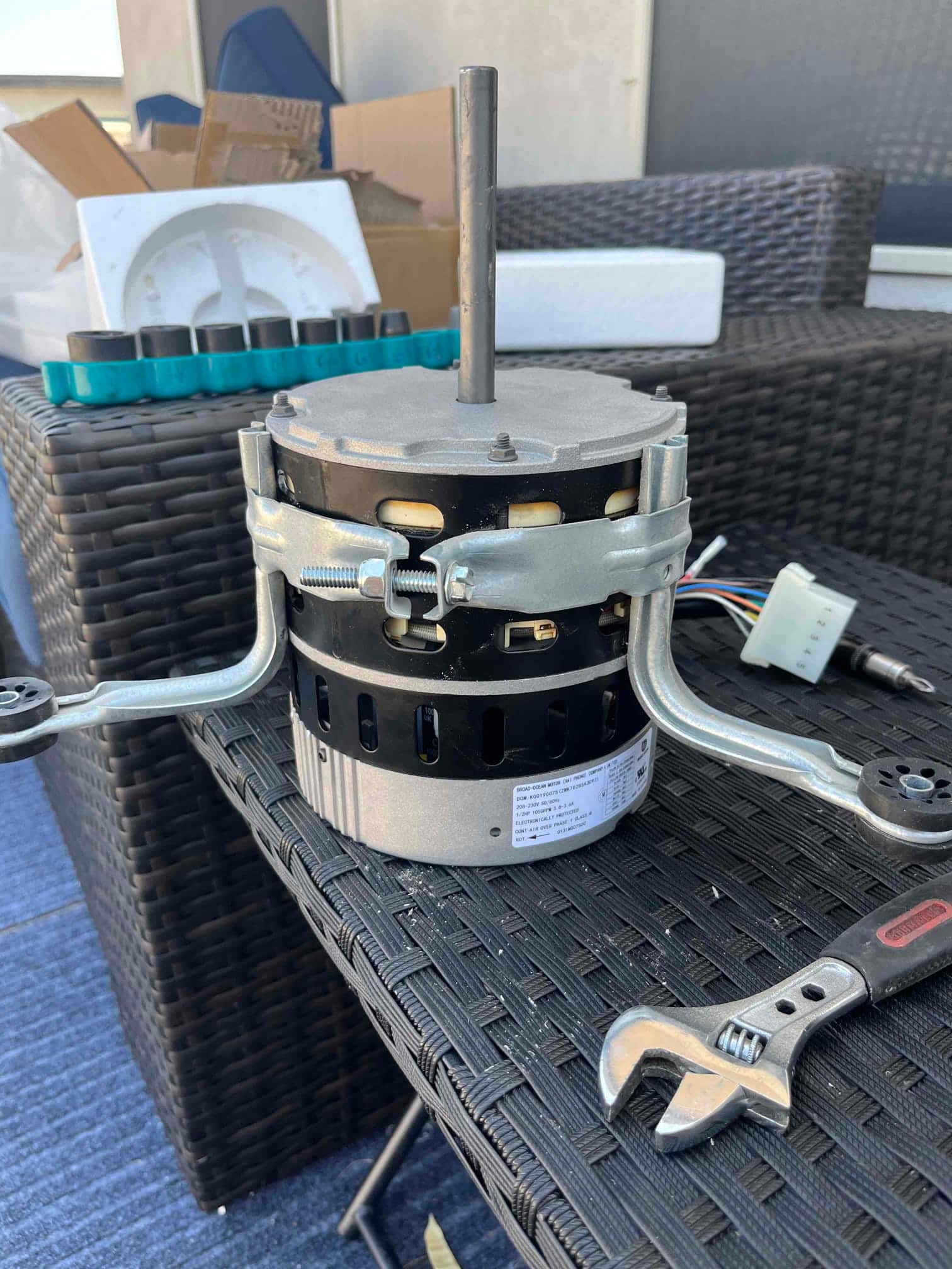 Indoor blower motor set on a work surface with mounting brackets attached and wiring connector visible beside a wrench.