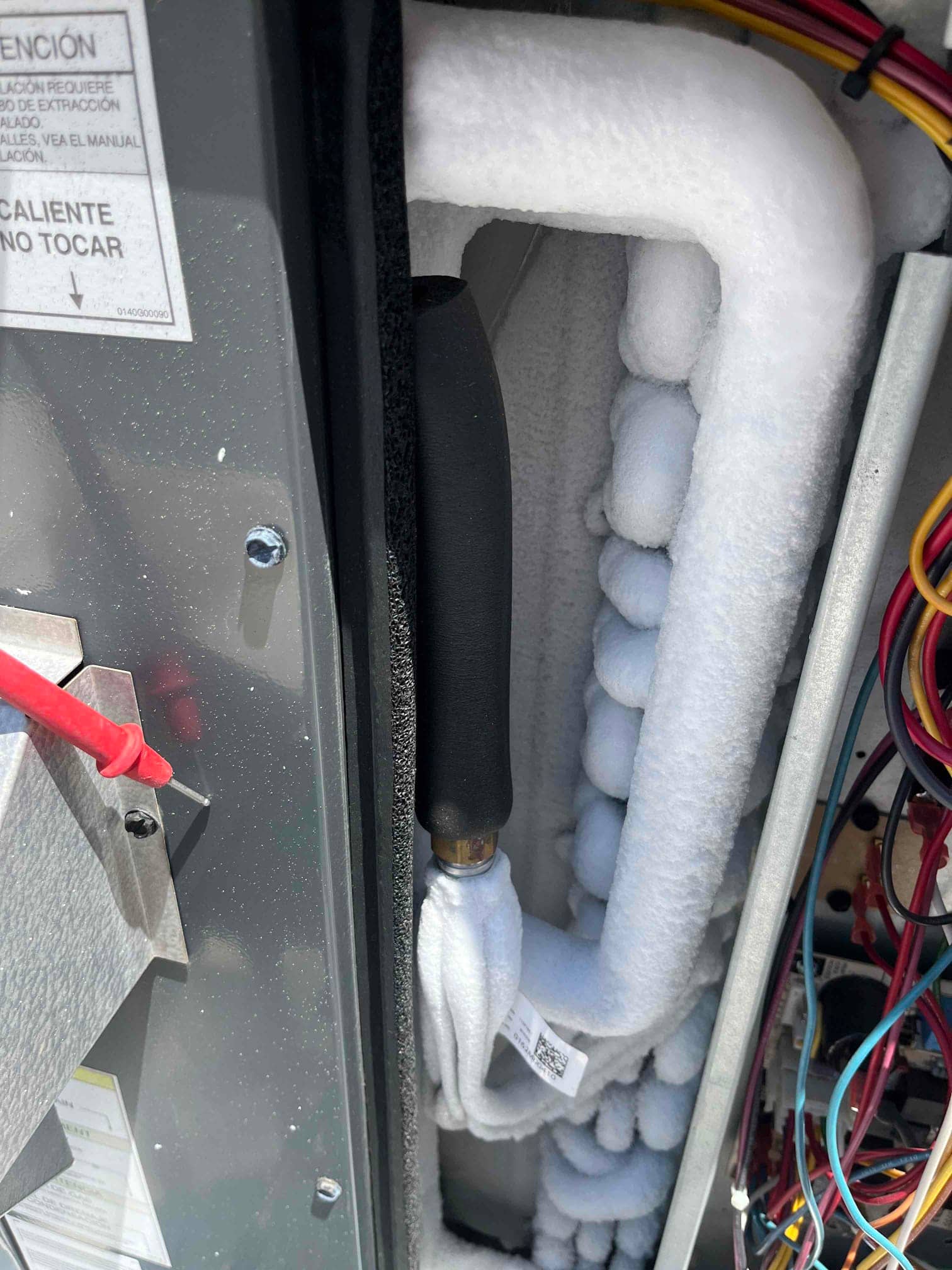 Indoor evaporator coil and suction line heavily frosted, with surrounding wiring visible inside the air handler cabinet.