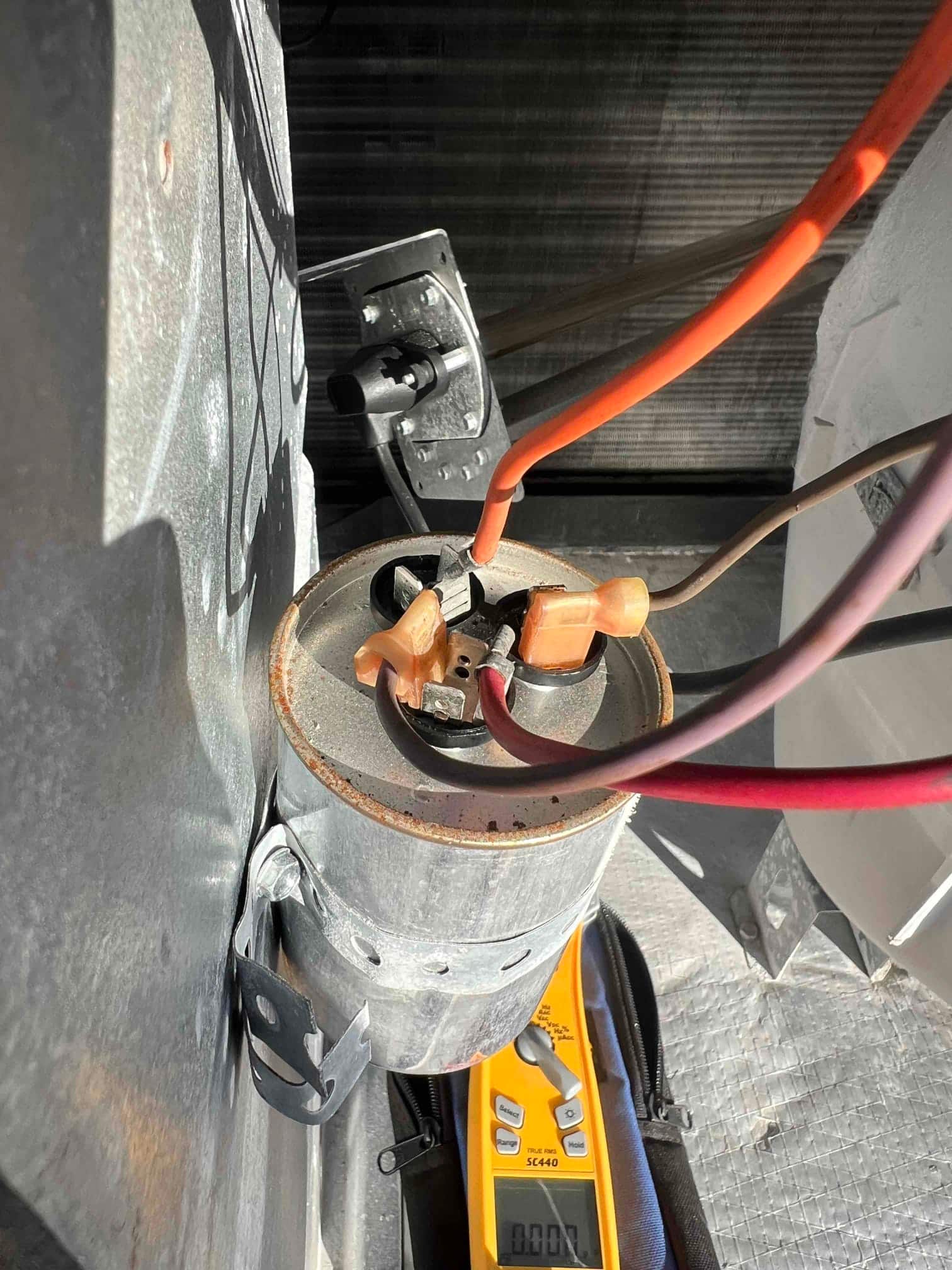 Installed dual run capacitor with connected compressor and fan wires, mounted in the outdoor condenser electrical compartment, showing clean terminals and secure bracket.