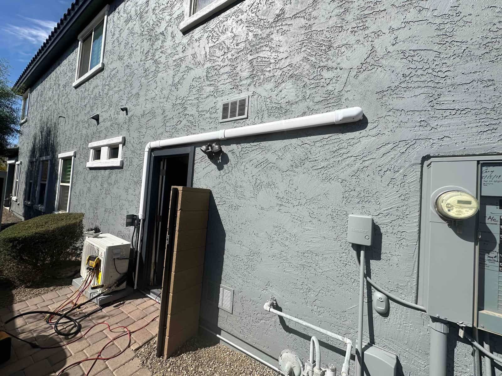 Mini-split outdoor unit set on a pad with insulated line hide installed along the exterior wall and electrical disconnect nearby.