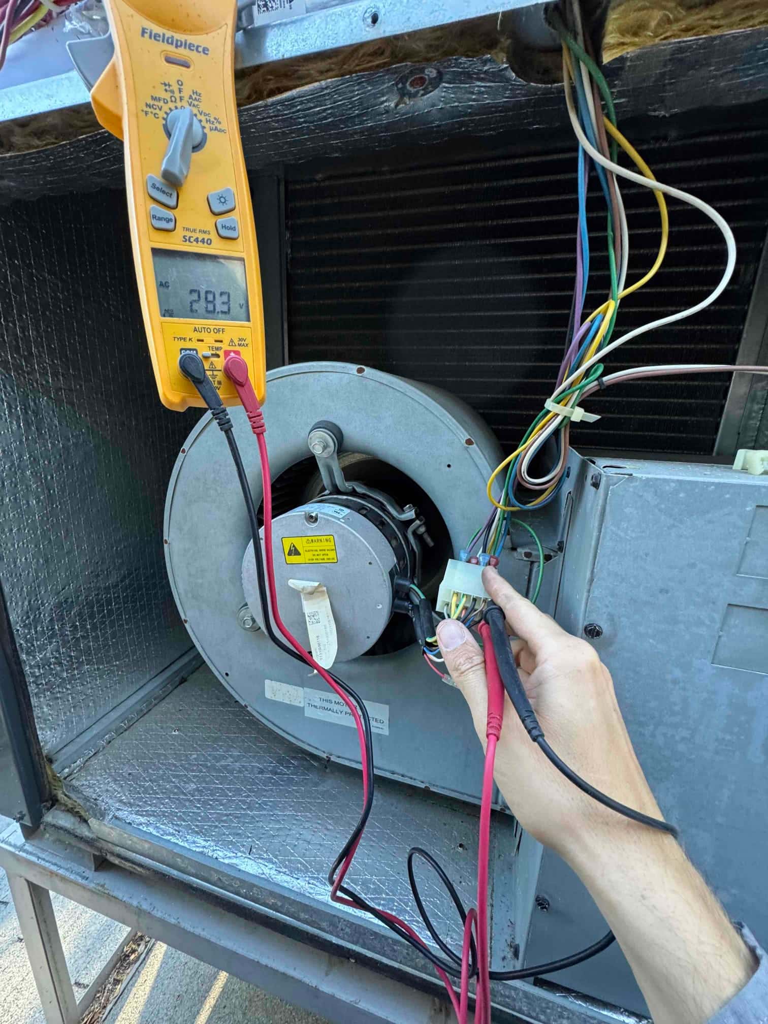 Multimeter measures 28.3 V at the indoor blower motor wiring while leads contact the motor connector.