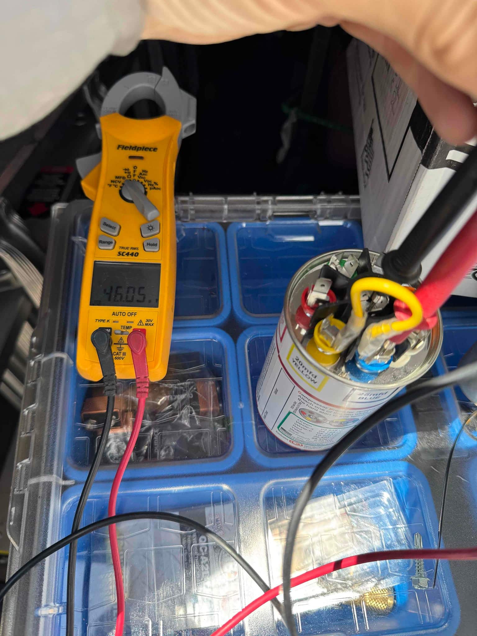 Multimeter measures capacitance at 46.05 μF on the dual-run capacitor with test leads connected to its terminals.
